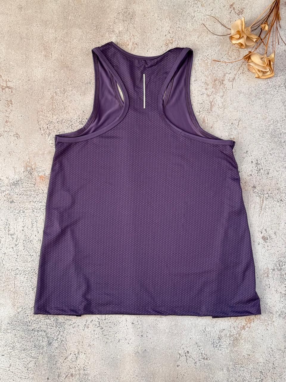 Camiseta deportiva morada sin mangas, extendida sobre una superficie beige con textura