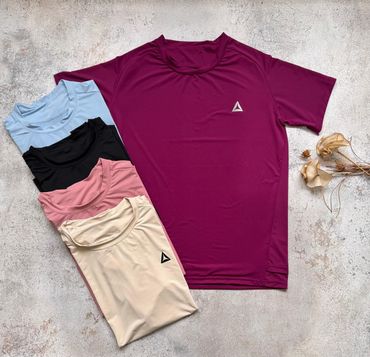 Varias camisetas deportivas dobladas en azul, negro, rosa, beige y burdeos sobre una superficie texturizada