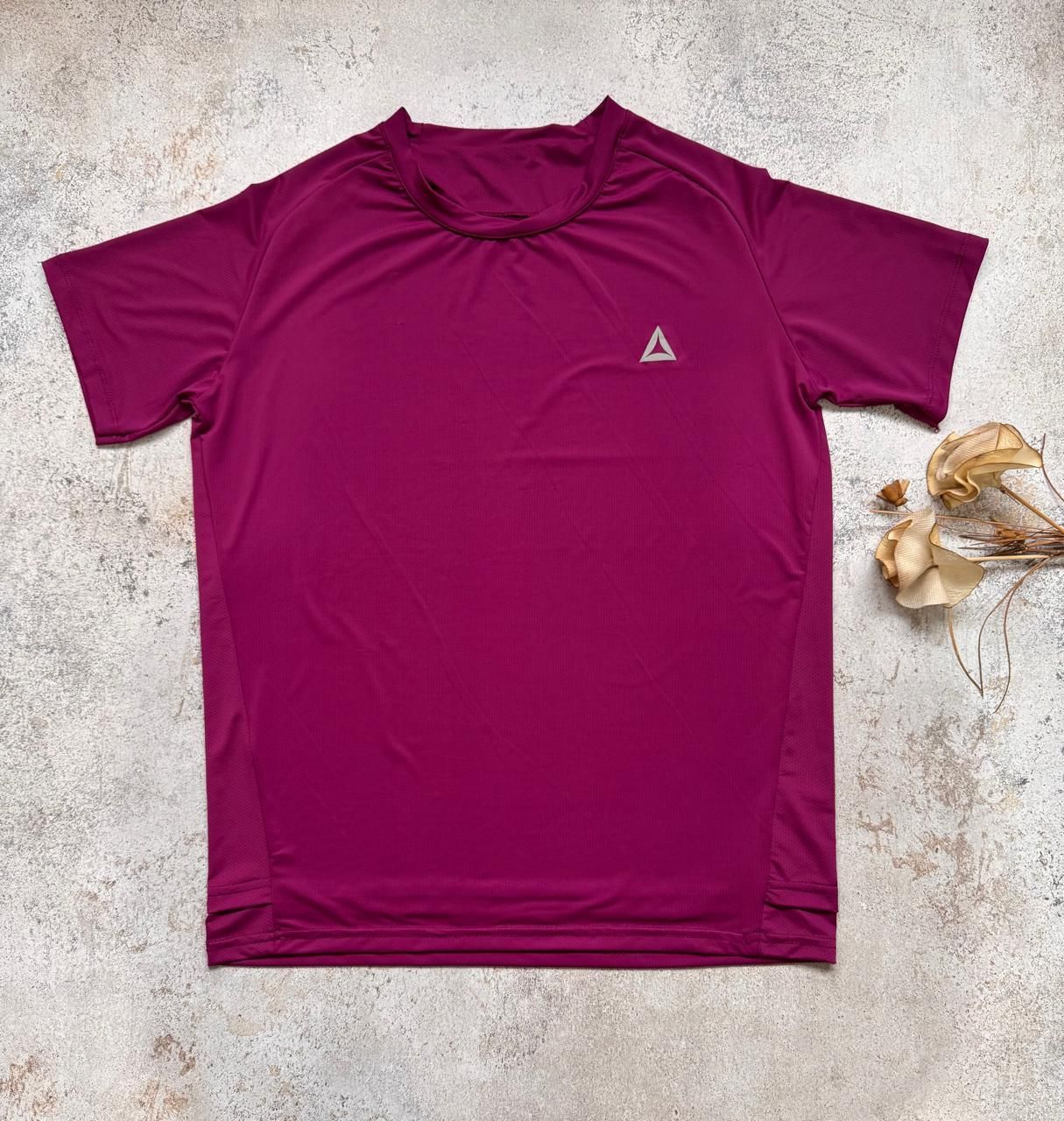 Camiseta deportiva magenta de manga corta extendida sobre una superficie clara con textura