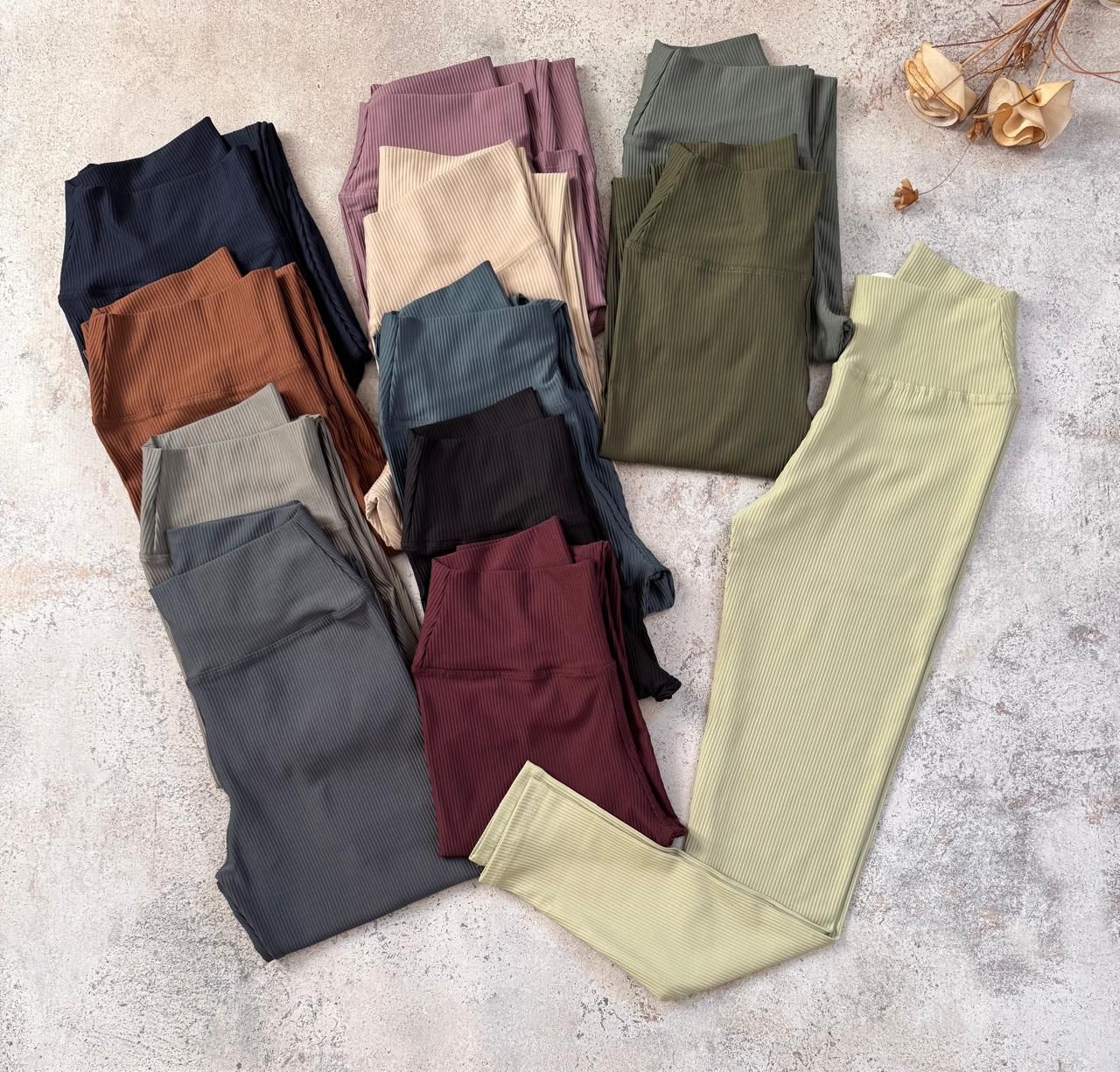 Pila de leggings acanalados doblados en varios tonos apagados sobre una superficie clara.
