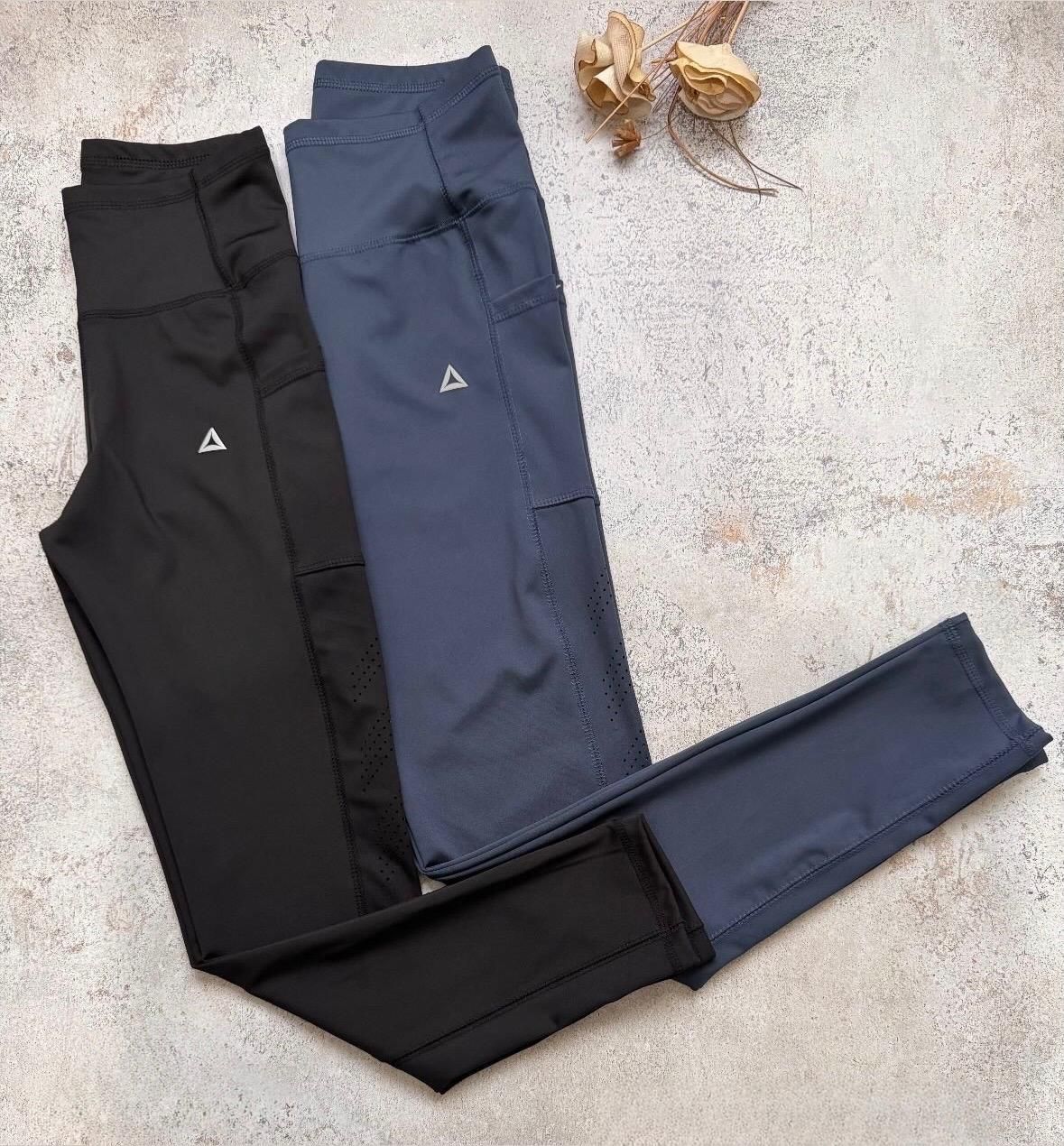 Dos pares de pantalones deportivos ajustados, uno negro y otro azul marino, colocados sobre una superficie de hormigón claro.