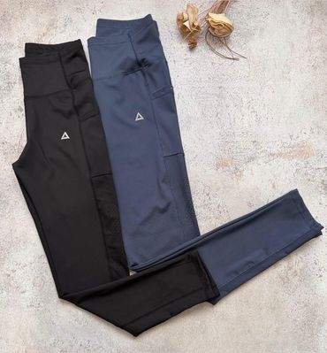 Dos pares de pantalones deportivos ajustados, uno negro y otro azul marino, colocados sobre una superficie de hormigón claro.