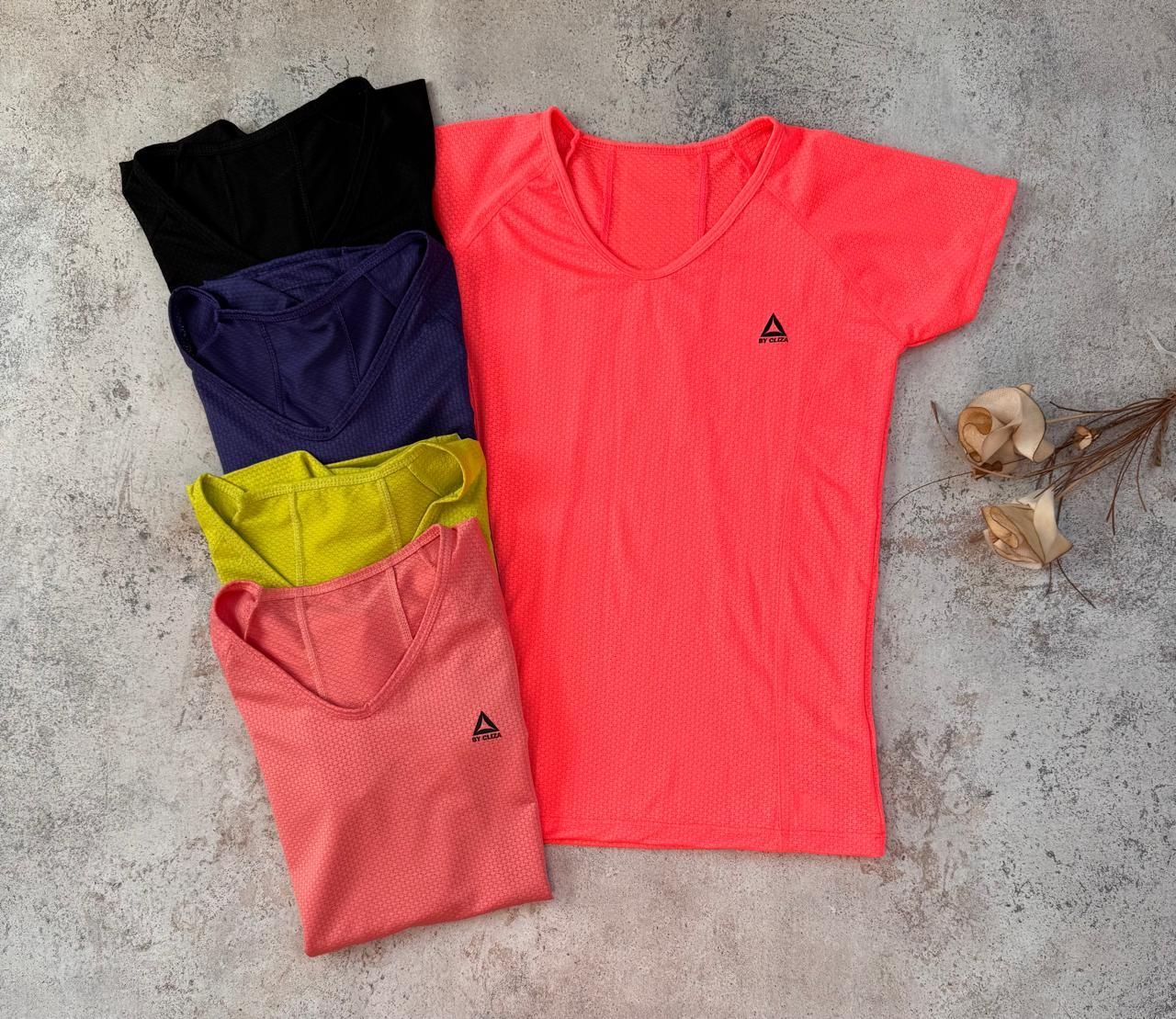 Cuatro camisetas de colores dobladas —negra, morada, amarilla y coral— y una camiseta coral