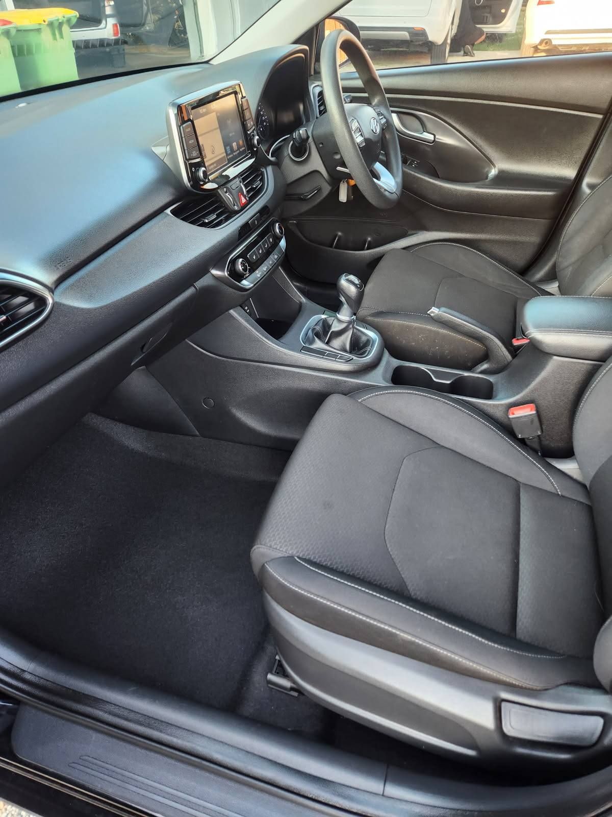 Interior view of a black car with dark gray cloth seats, showing dashboard, console, and steering wheel.