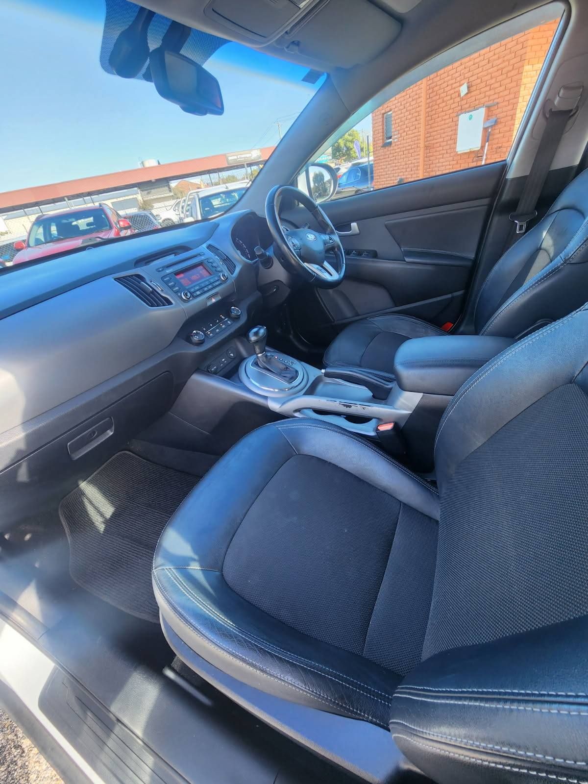 Interior view of a Kia Sportage showing black leather seats, dashboard, steering wheel, and gear shift.