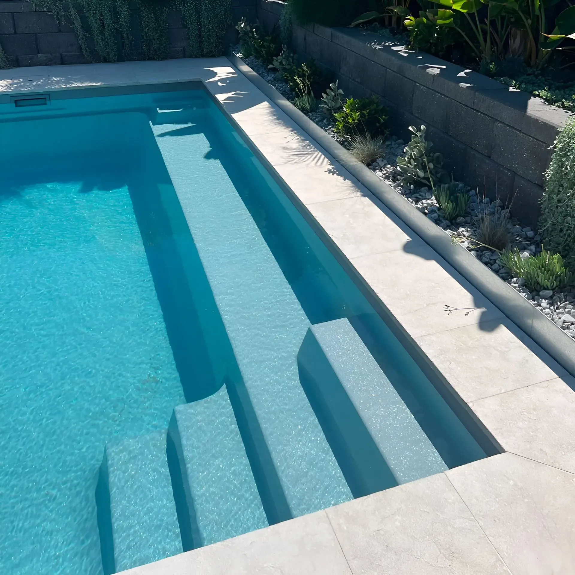 Blue Swimming Pool With Built-in Steps and a Stone Deck Beside a Planter Wall — Billabong Pool Co in Smeaton Grange, NSW