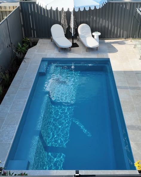 Backyard Pool With Two White Lounge Chairs and a Striped Umbrella Beside a Gray Fence — Billabong Pool Co in Wollongong, NSW