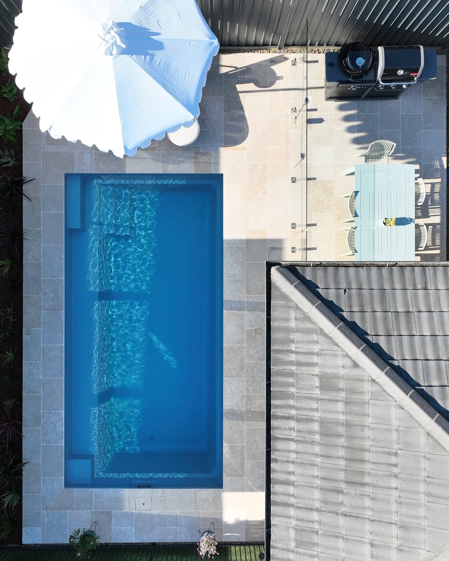 Aerial View of a Backyard With a Blue Swimming Pool, White Patio Umbrella, Deck Chairs, and Patio Furniture — Billabong Pool Co in Wollongong, NSW