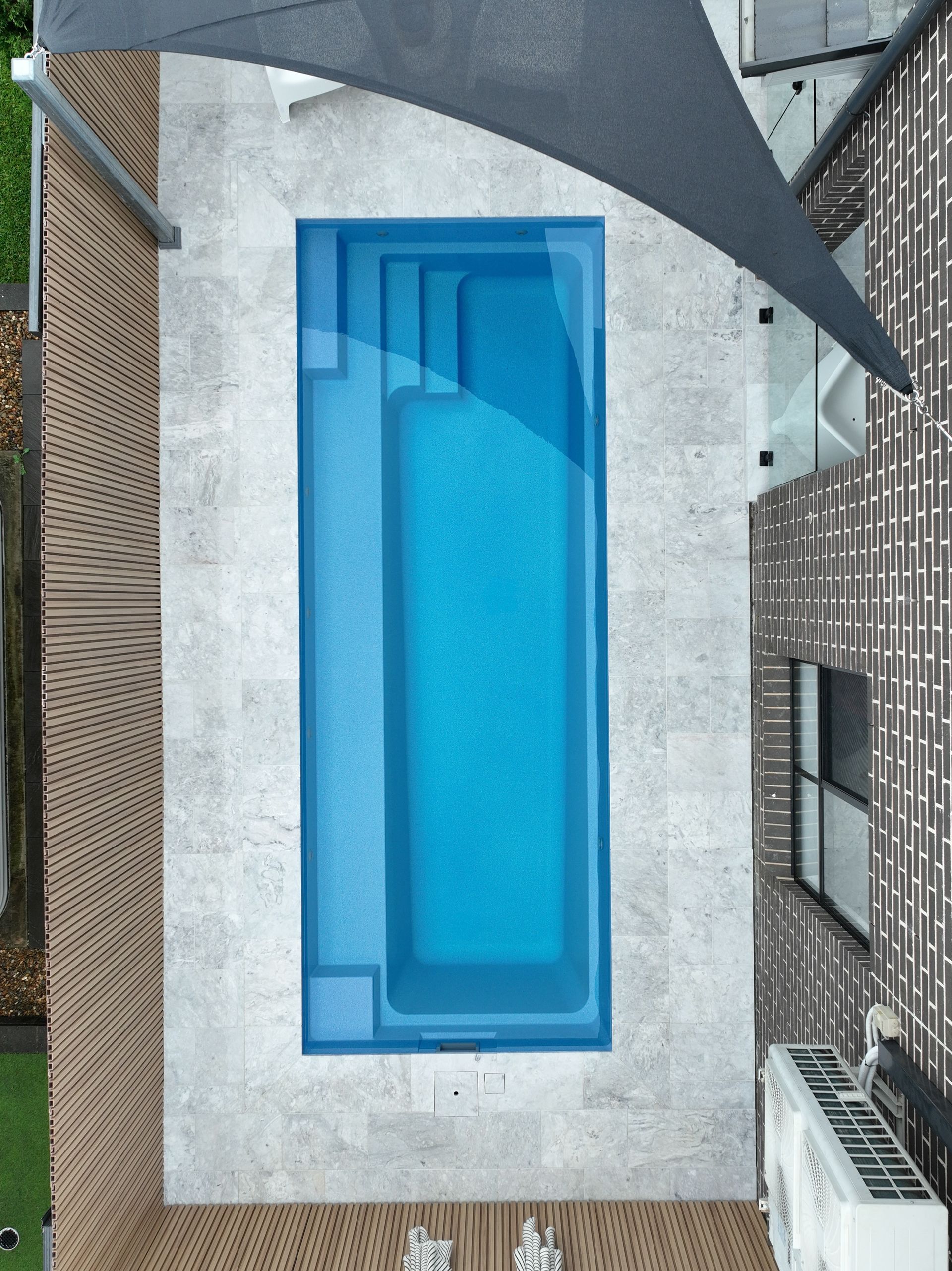 An Aerial View of A Narrow, Rectangular Blue Swimming Pool Surrounded — Billabong Pool Co in Smeaton Grange, NSW