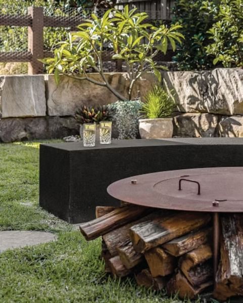 A Pile of Logs Is Sitting in The Grass Next to A Fire Pit — Billabong Pool Co in Smeaton Grange, NSW