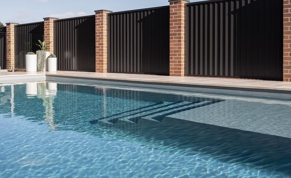 Outdoor Swimming Pool With Blue Water Beside a Brick Wall and Black Privacy Fences — Billabong Pool Co in Smeaton Grange, NSW