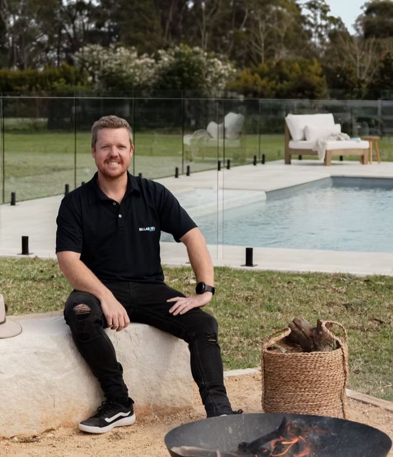 A Man Is Sitting on A Bench Next to A Fire Pit — Billabong Pool Co in Smeaton Grange, NSW