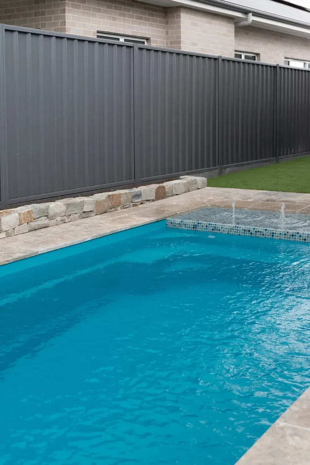 Turquoise Swimming Pool Beside a Stone Deck and Dark Gray Fence in a Backyard — Billabong Pool Co in Smeaton Grange, NSW