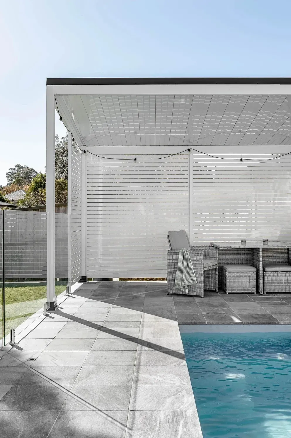 Covered Patio Beside a Swimming Pool With Lounge Chairs and a White Slatted Wall — Billabong Pool Co in Smeaton Grange, NSW