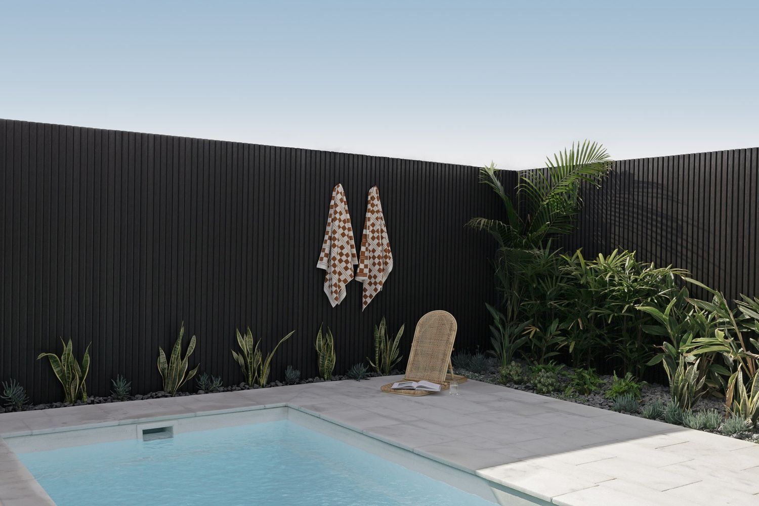 Backyard Pool With Black Fence, Plants, and a Woven Chair on a Tiled Patio — Billabong Pool Co in Smeaton Grange, NSW