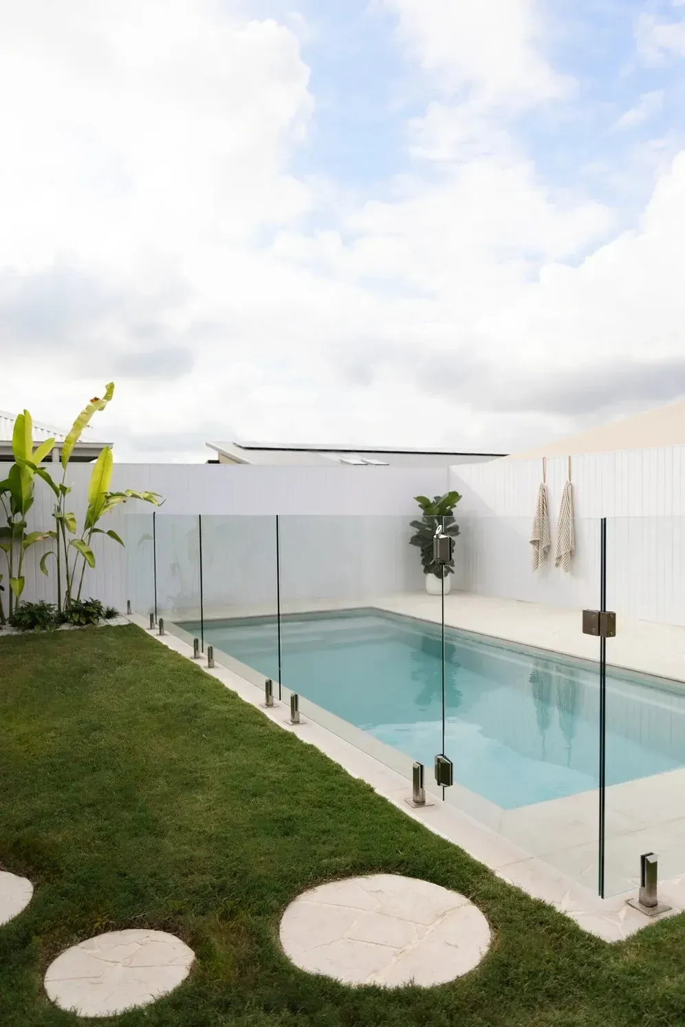 Modern Backyard Pool With Glass Fence, Green Lawn, and Cloudy Sky — Billabong Pool Co in Smeaton Grange, NSW