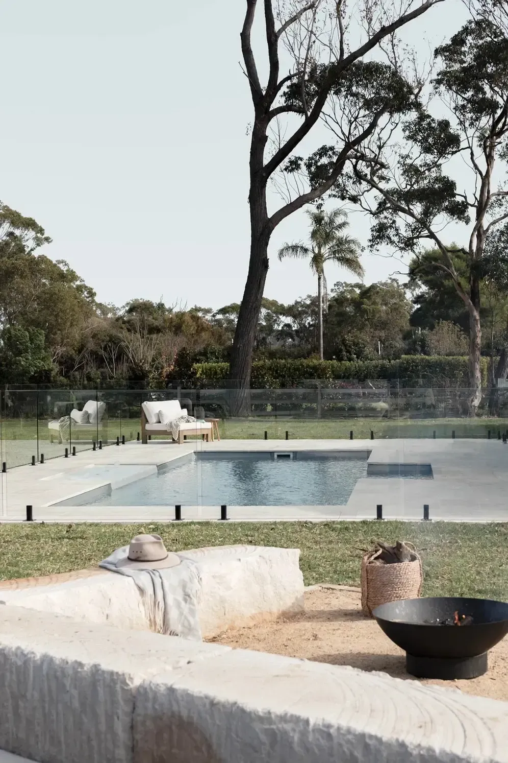Backyard Pool With Lounge Chairs, Fire Pit, and Tall Trees Beyond a Glass Fence — Billabong Pool Co in Smeaton Grange, NSW