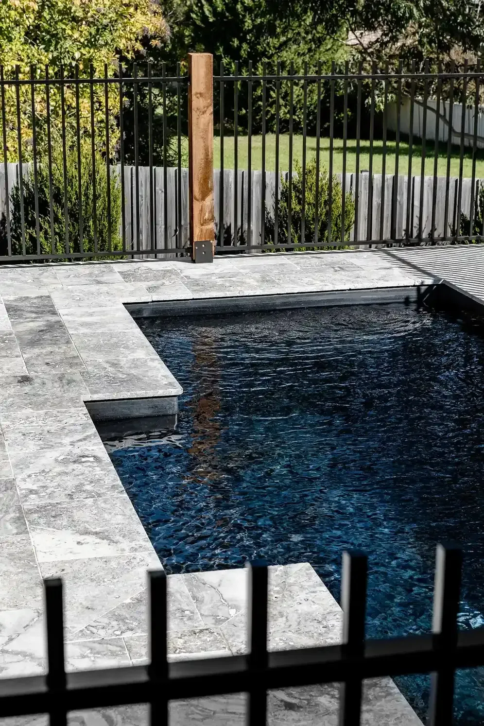 Backyard Pool With Dark Water, Stone Deck, and Black Fence Overlooking Greenery — Billabong Pool Co in Smeaton Grange, NSW
