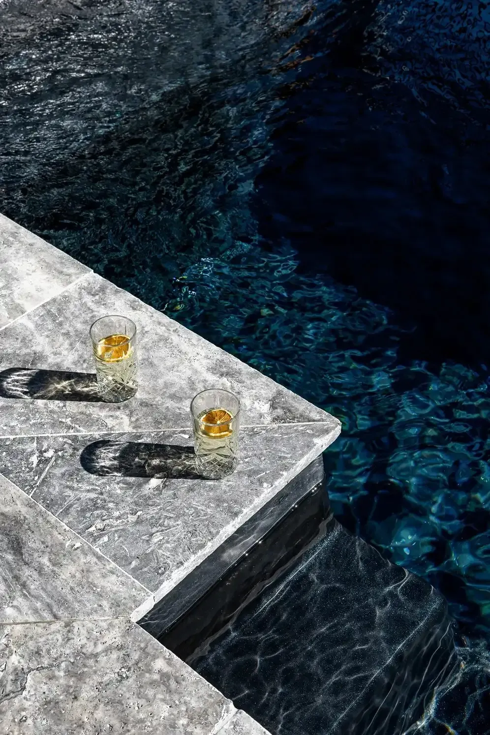 Two Drinks on a White Stone Ledge Beside Dark Blue Pool Water — Billabong Pool Co in Smeaton Grange, NSW