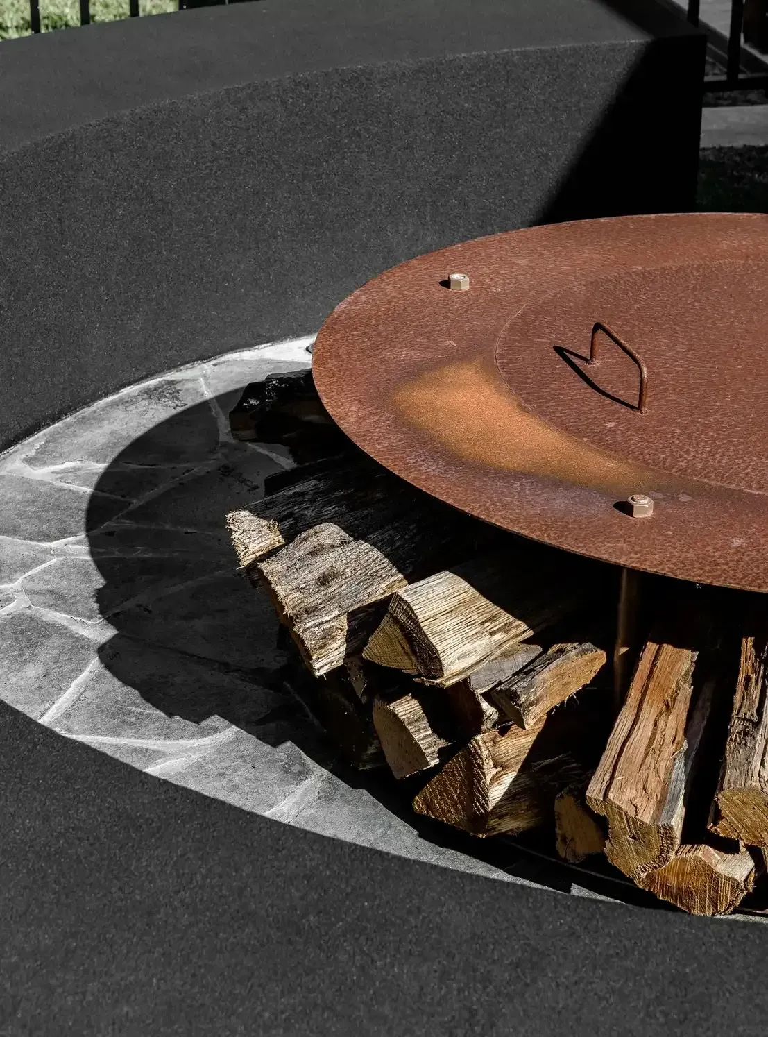 Rusty Metal Fire Pit Filled With Logs, Set in a Black Outdoor Surface — Billabong Pool Co in Smeaton Grange, NSW