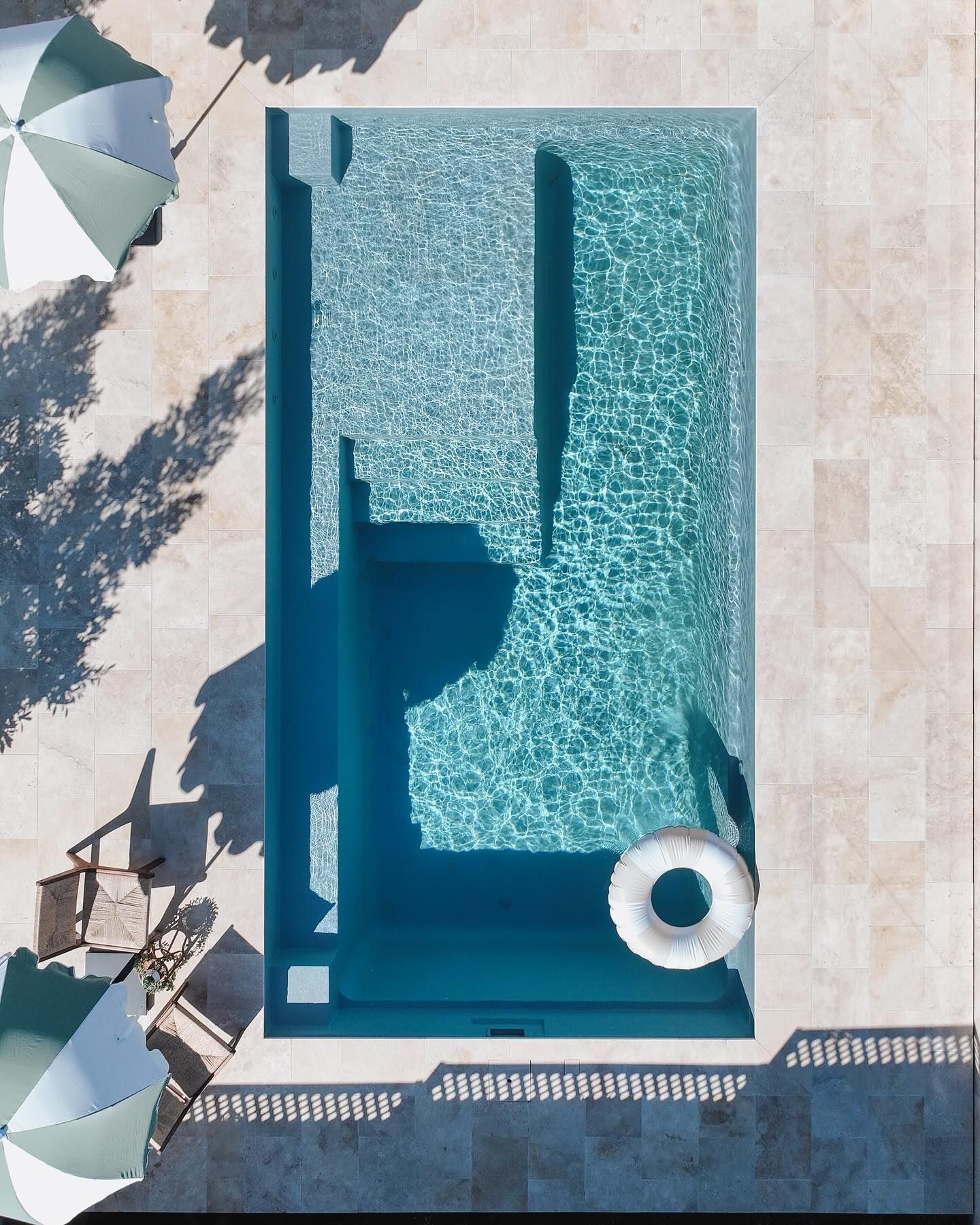 Top-down view of a rectangular turquoise pool with lounge chairs and umbrellas on a sunlit terrace
