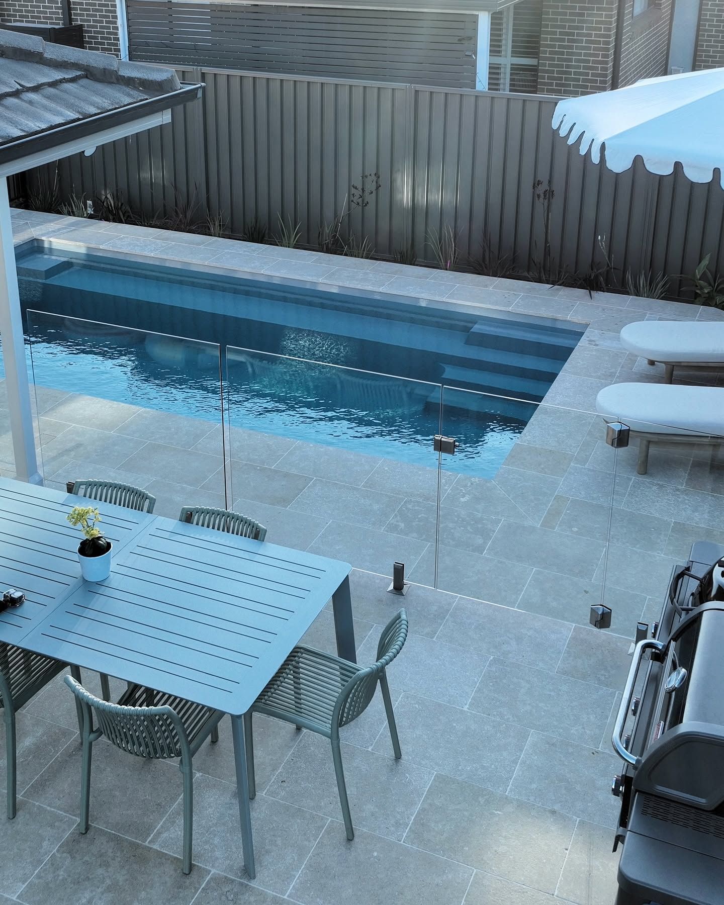 Snowy Backyard Patio With a Small Rectangular Swimming Pool, Table, Chairs, and Lounge Chairs Beside a Wooden Fence — Billabong Pool Co in Wollongong, NSW