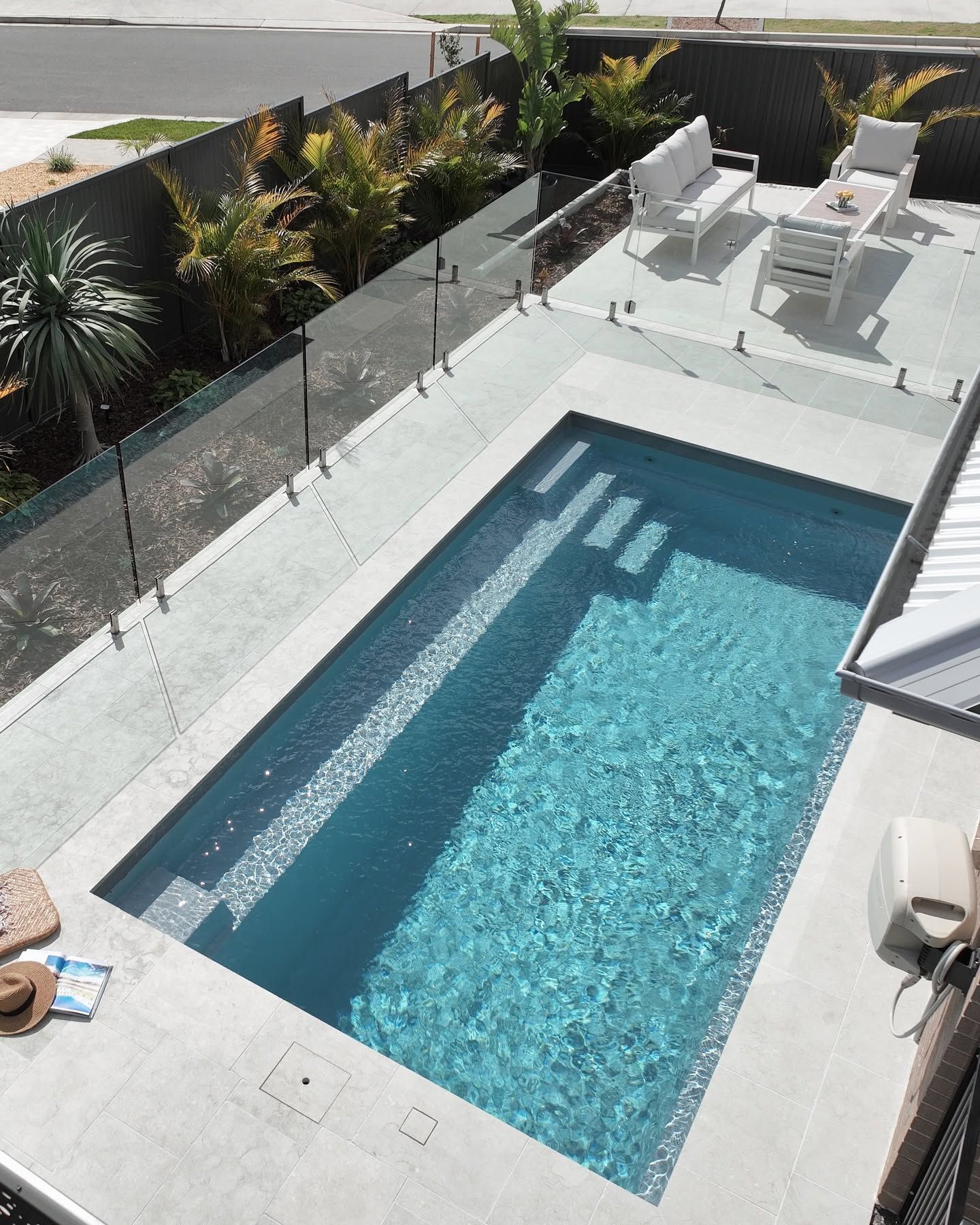 Modern Backyard With a Rectangular Blue Pool, Glass Fence, and White Patio Furniture Under Bright Sun — Billabong Pool Co in Wollongong, NSW