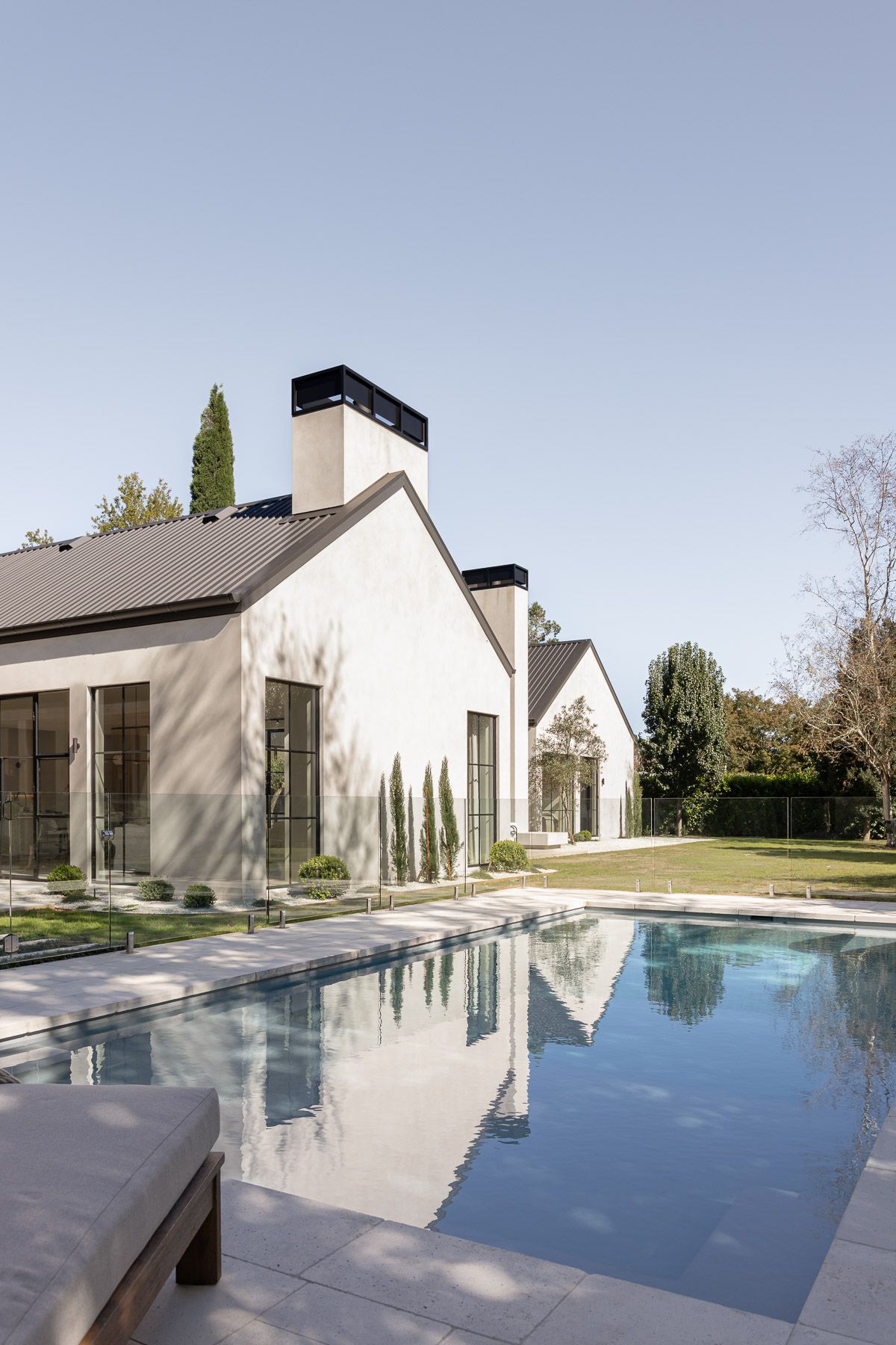 Modern house with white walls beside a reflective swimming pool under a clear sky — Billabong Pool Co in Smeaton Grange, NSW