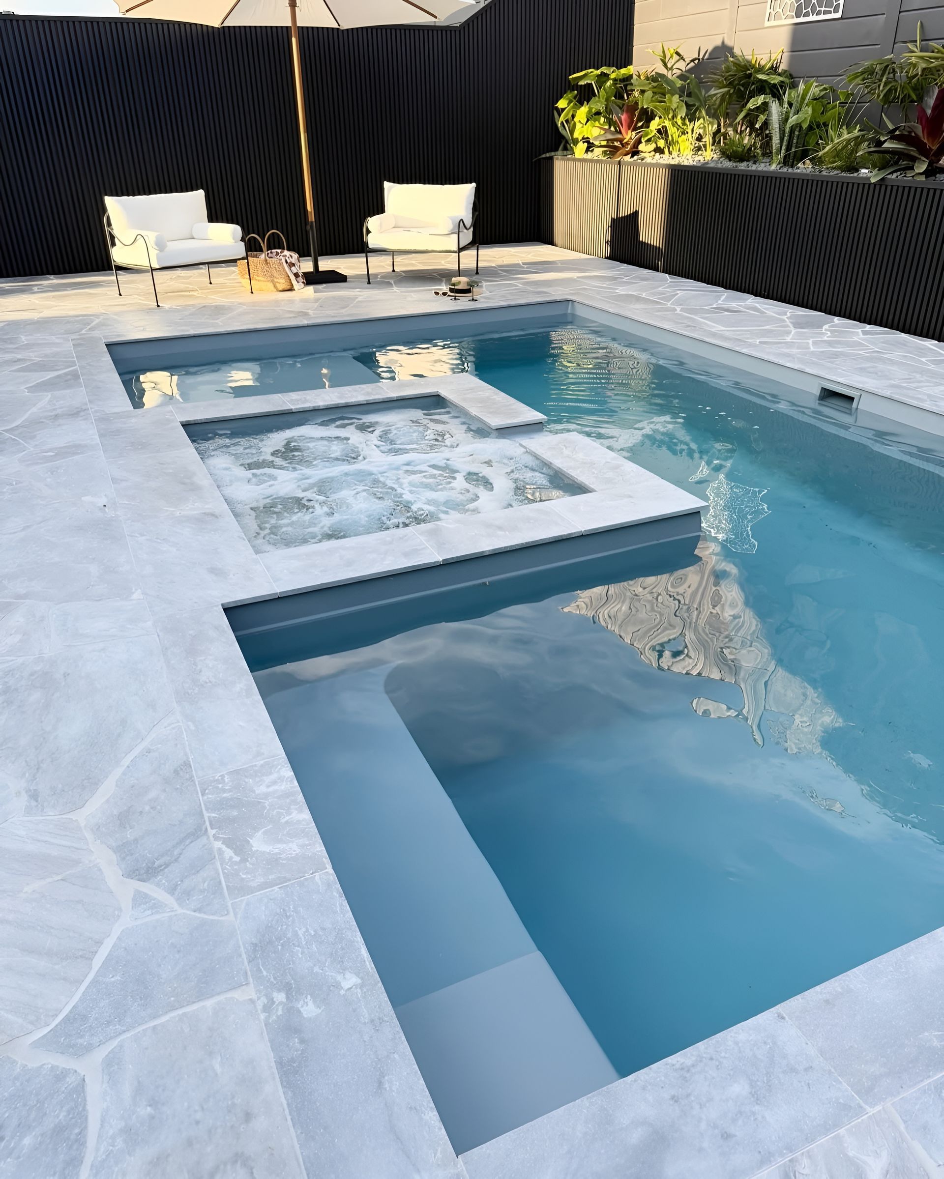 Modern Backyard Pool With a Sun Shelf, SPA Seating, and Two Lounge Chairs Beside Black Fencing — Billabong Pool Co in Wollongong, NSW