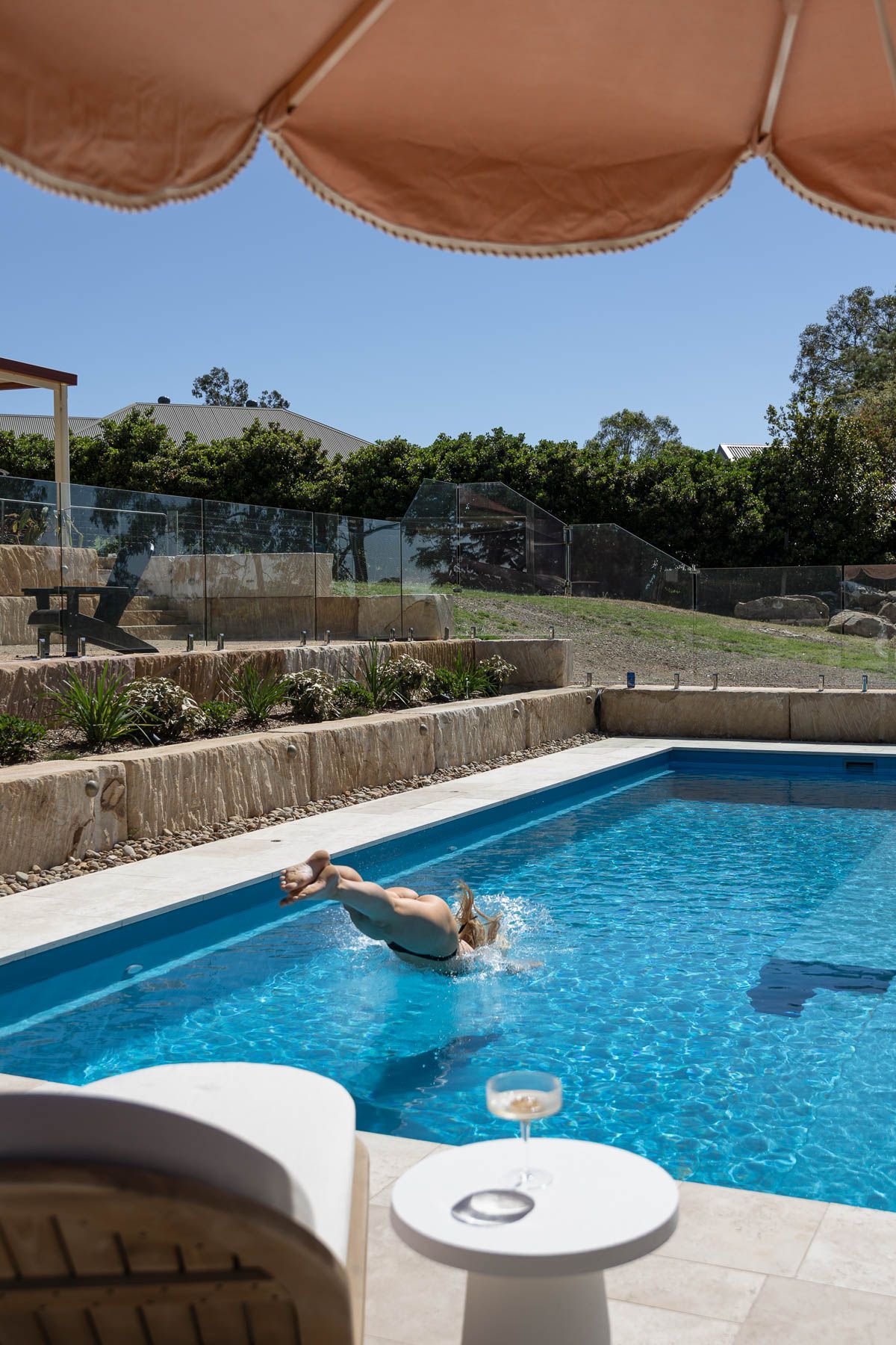 Person Floating in a Bright Blue Swimming Pool Under a Tan Patio Umbrella — Billabong Pool Co in Smeaton Grange, NSW