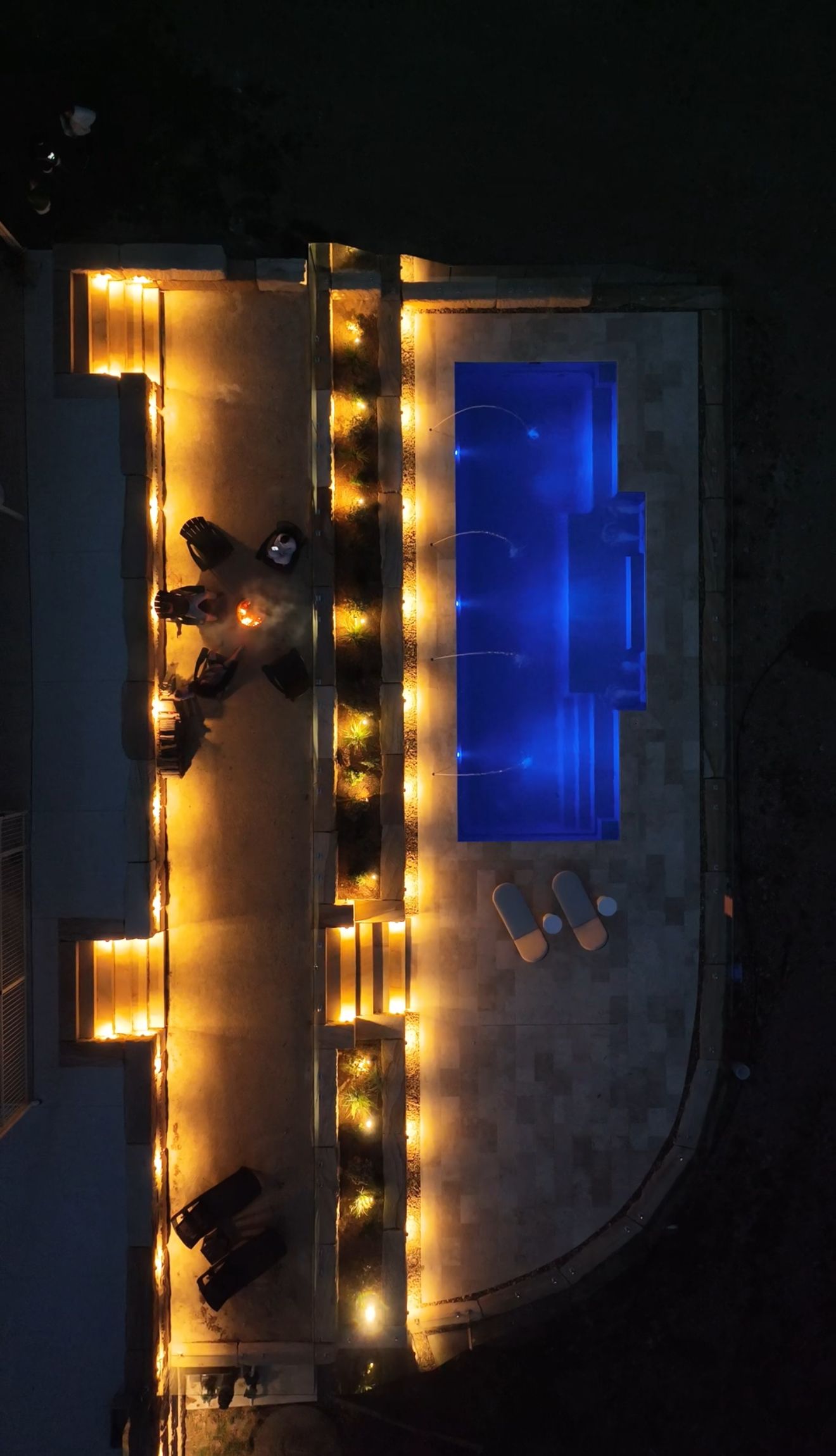 Nighttime Aerial View of a Lit Poolside Patio With Blue Water — Billabong Pool Co in Smeaton Grange, NSW