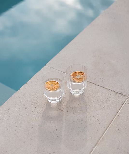Two clear glasses with orange slices on a white tiled surface next to a pool — Billabong Pool Co in Smeaton Grange, NSW