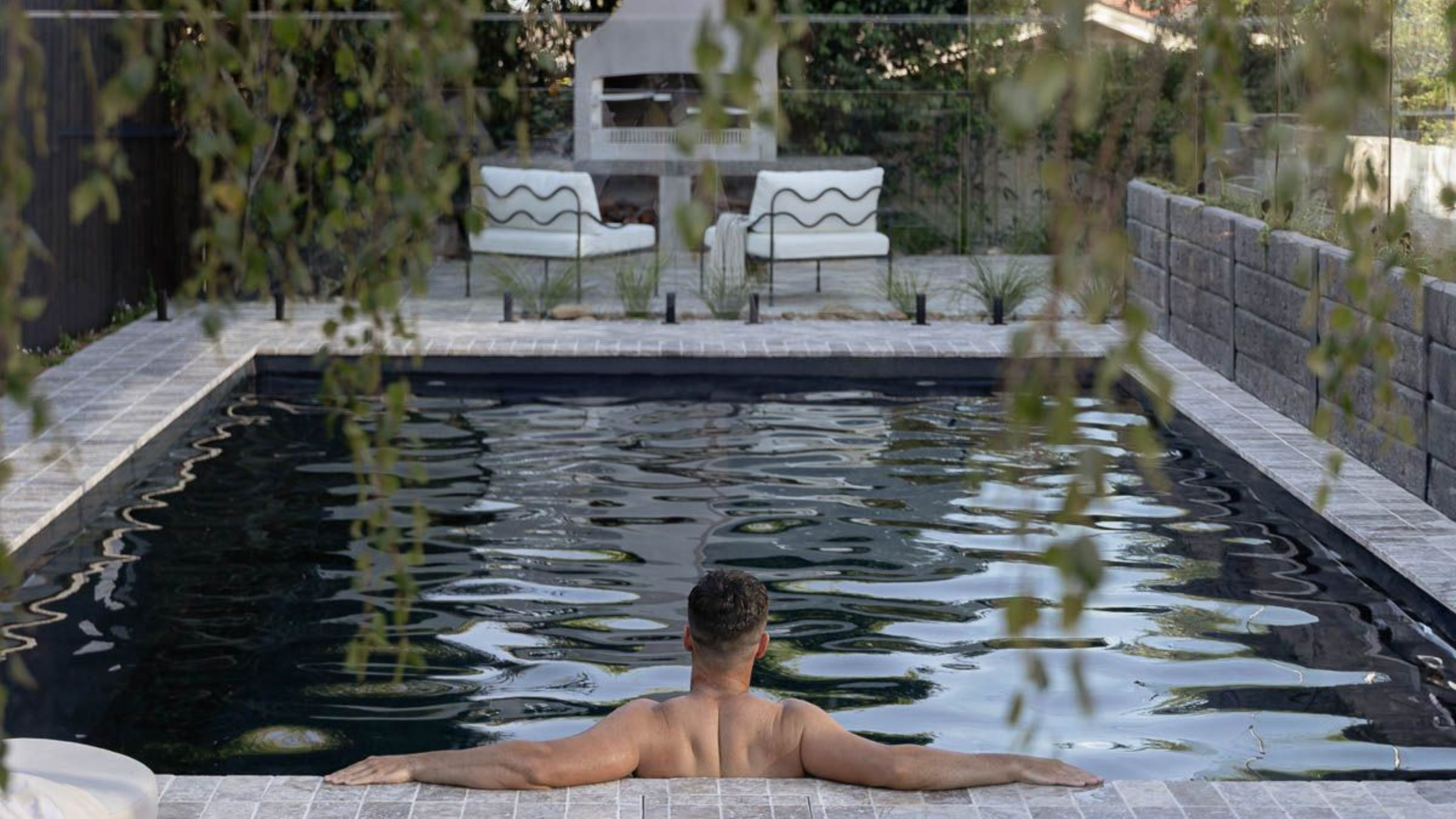 Person relaxing in a narrow backyard pool with arms outstretched, surrounded by stone walls and greenery — Billabong Pool Co in Smeaton Grange, NSW