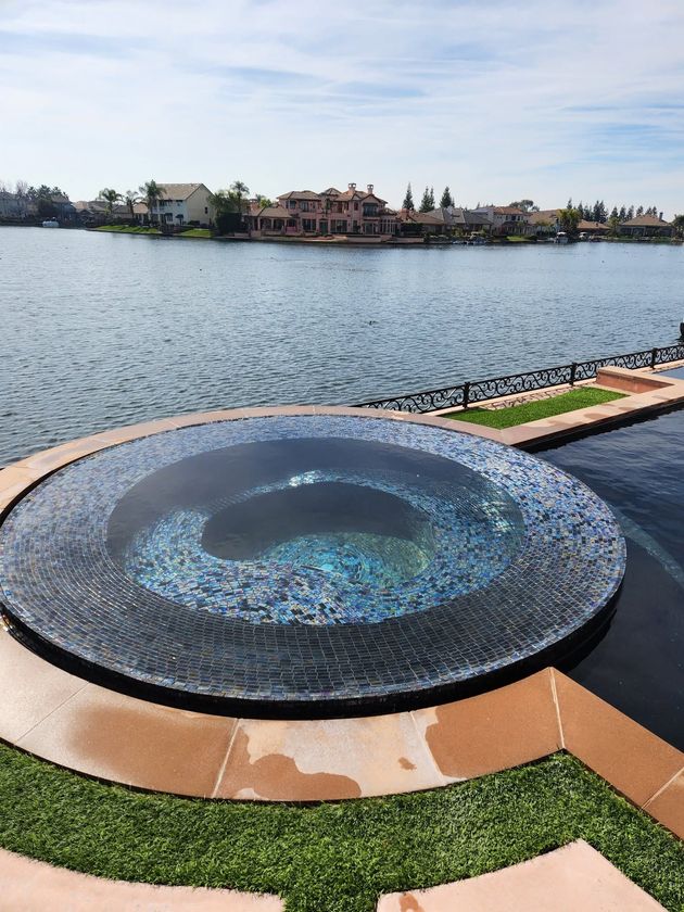 Circular mosaic fountain by a lake, with waterfront homes in the distance and a landscaped path in front