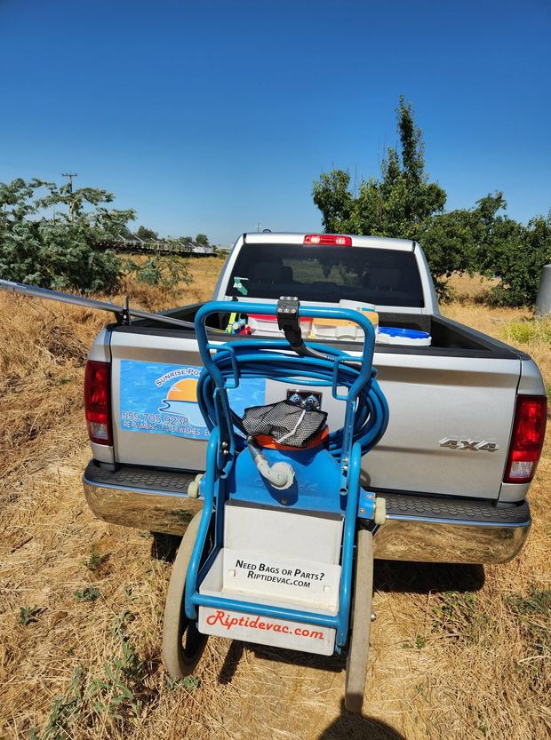 Blue sprayer mounted on a silver pickup truck in a dry field under a clear blue sky