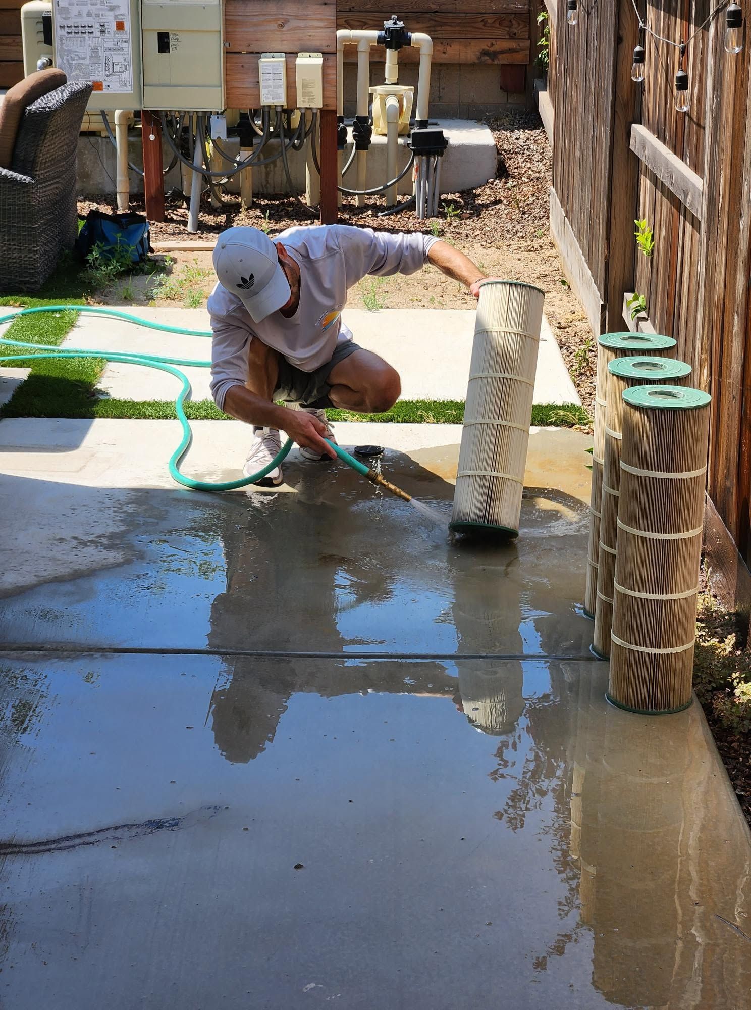 Worker kneeling on wet pavement spraying water near a post with a hose