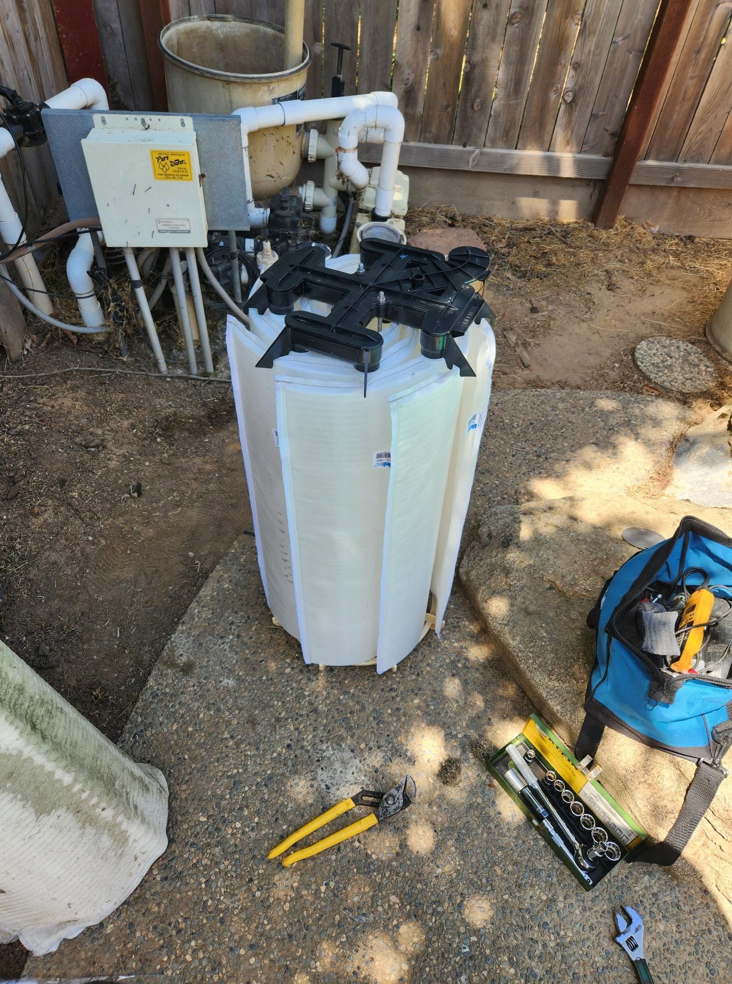 Outdoor HVAC unit and equipment in a yard, with tools scattered nearby and a fence in the background