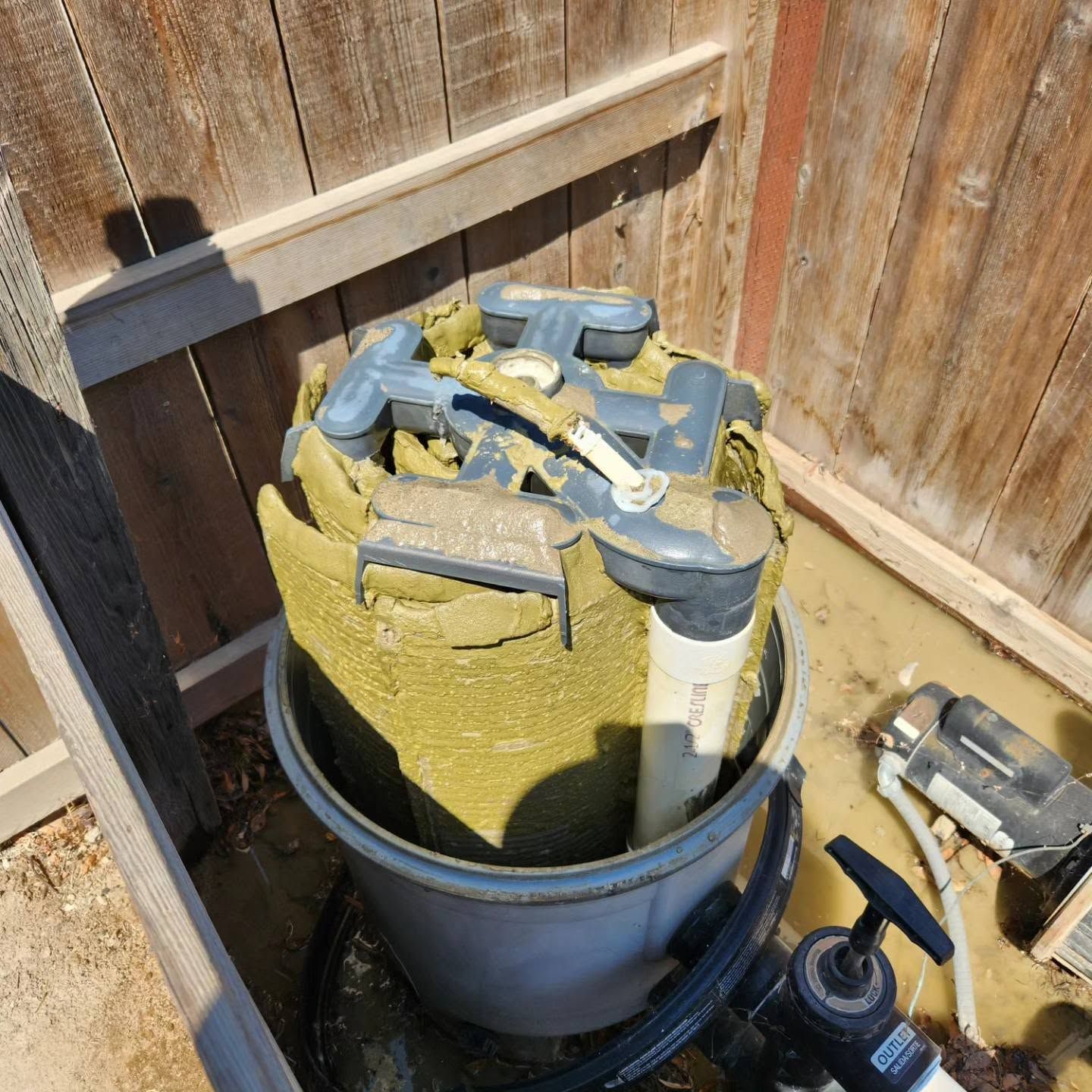 Large blue container filled with green foam and tools in a wooden fenced corner