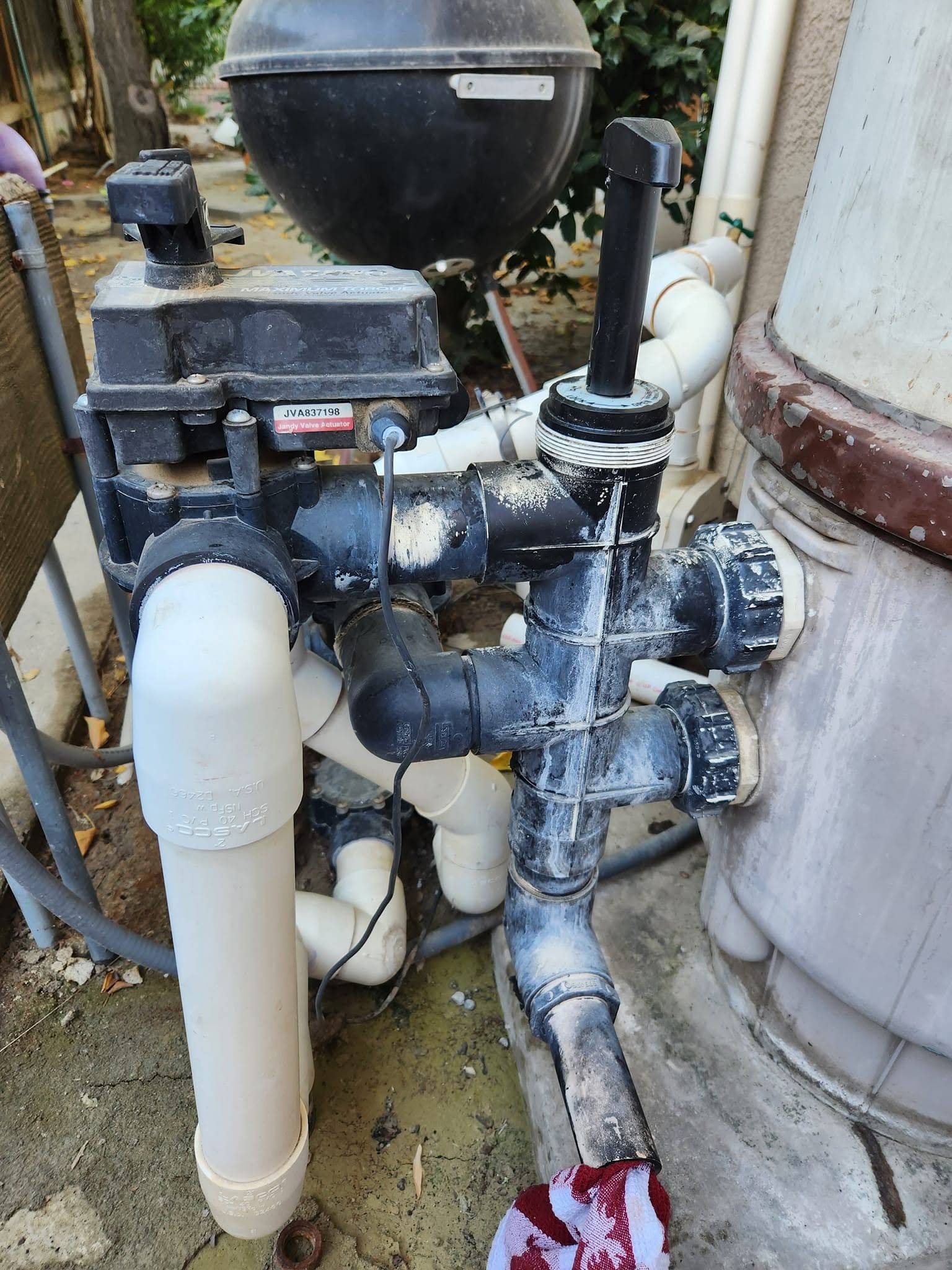 Pool pump and filter plumbing with black pipes and a white filter tank outdoors