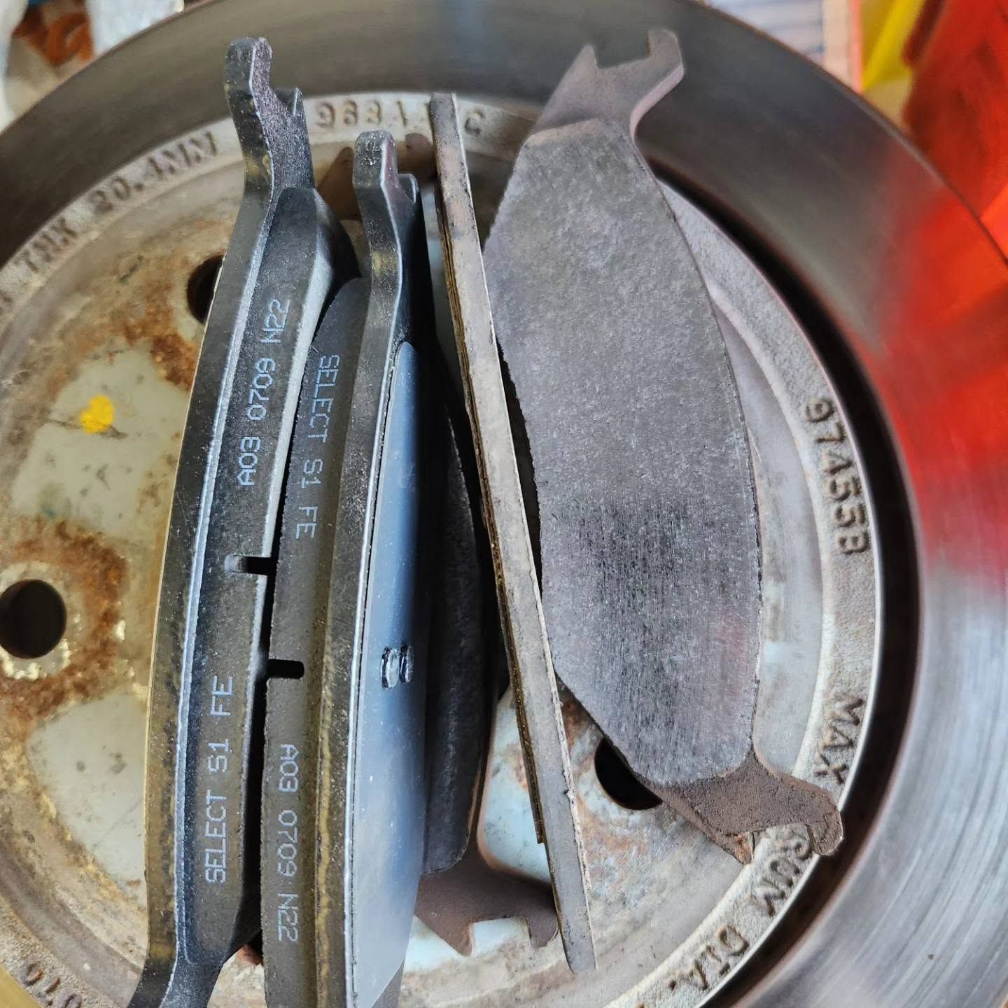 Close-up of worn car brake pads arranged around a metal brake rotor.