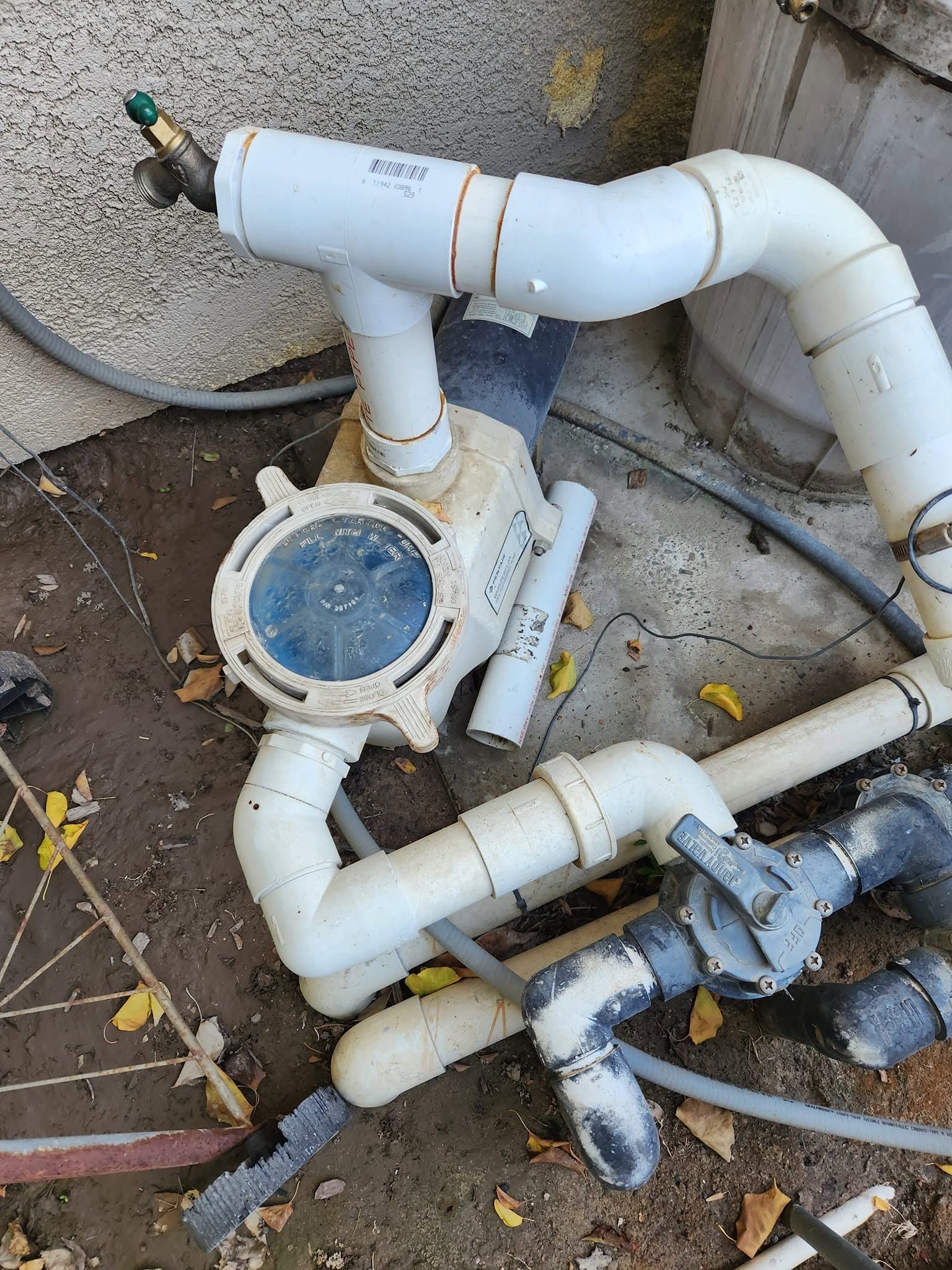White PVC pool plumbing with a round filter cap and connected pipes outdoors on the ground