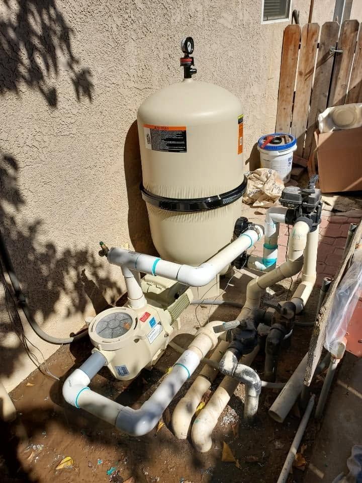 Outdoor pool pump and filter equipment with white PVC pipes beside a stucco wall.