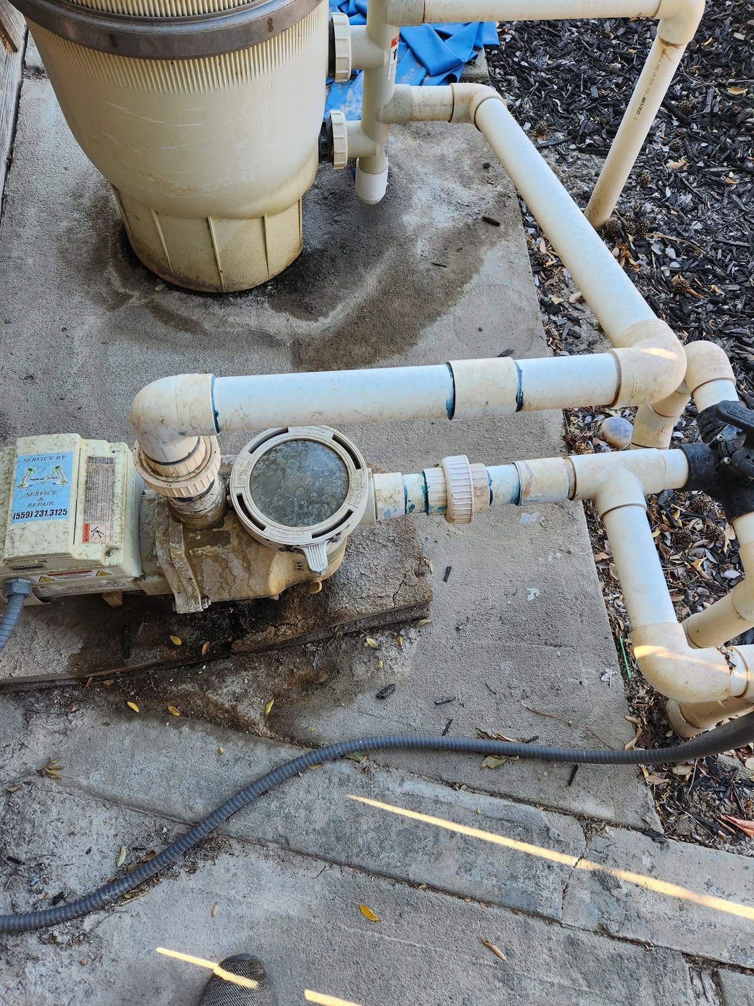 Pool pump and PVC pipes with a cracked joint and water leakage on a concrete surface.