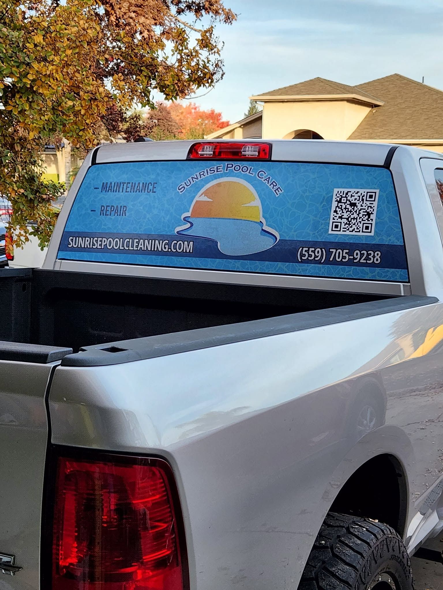 Blue pickup truck with business advertisement on rear window, including logo and QR code, parked outdoors