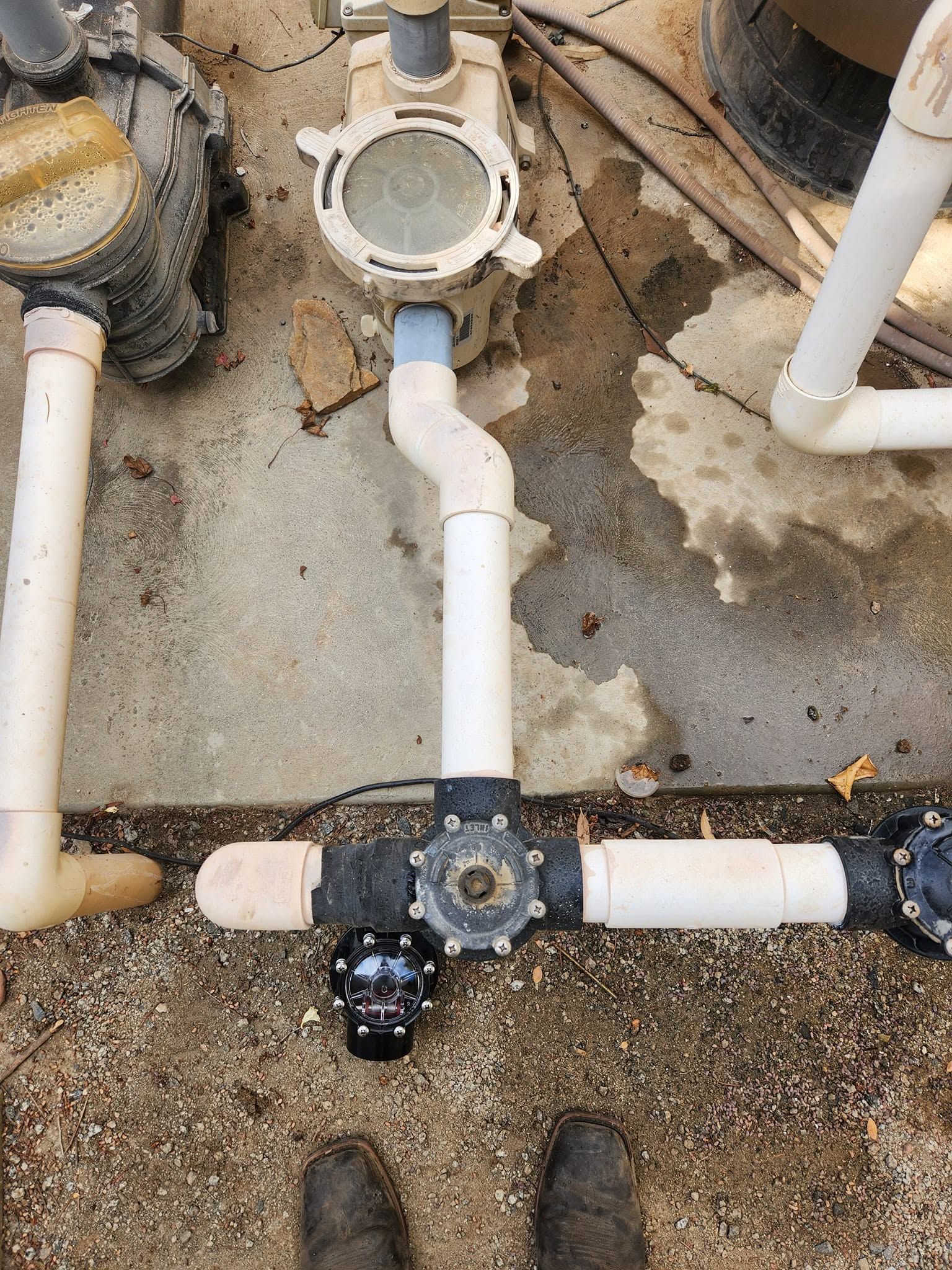 Outdoor pool plumbing with white PVC pipes, valves, and pump connections on concrete ground
