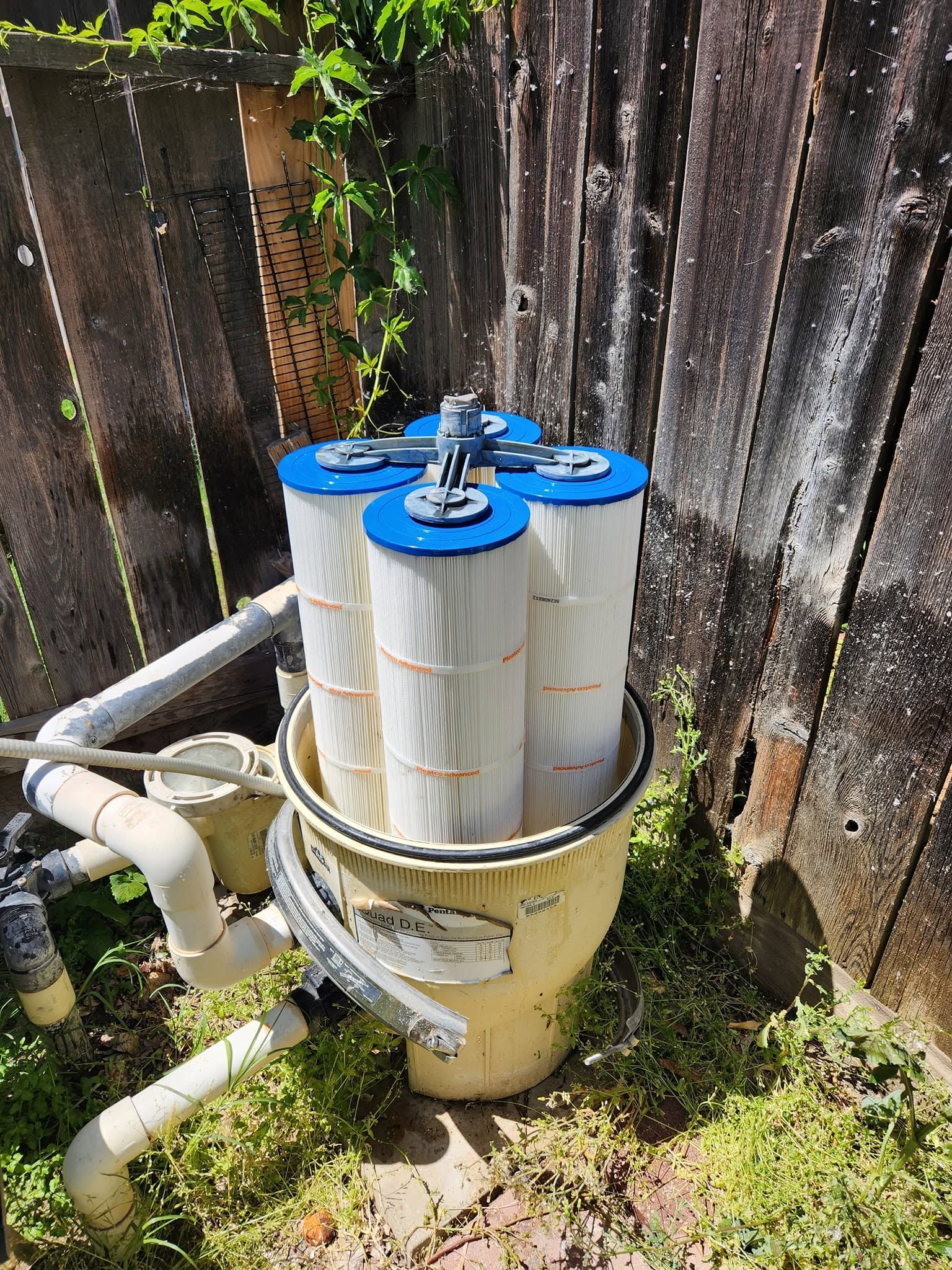 Blue water filter tank and pipes beside a weathered wooden fence outdoors