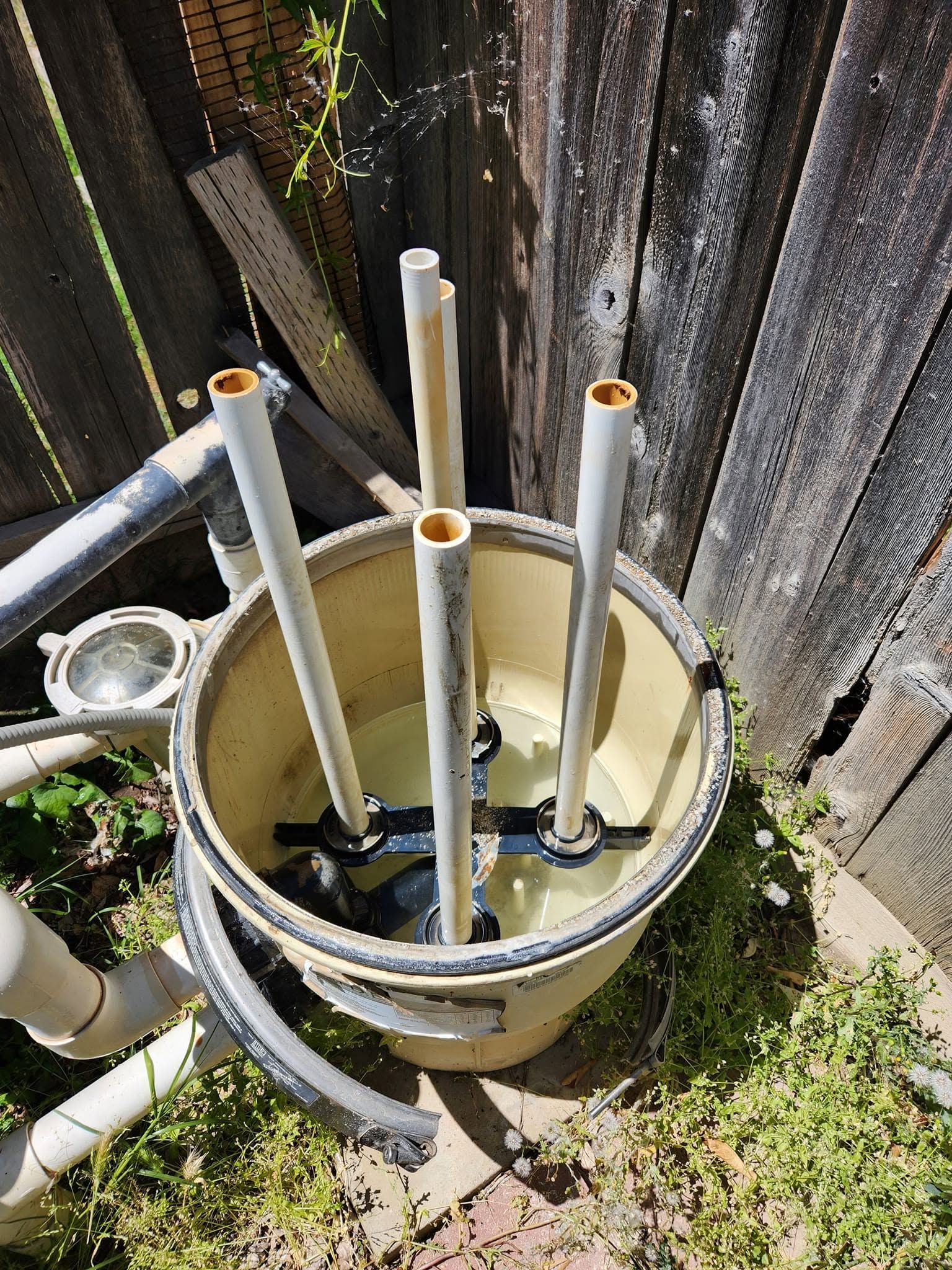 Open utility pit with pipes and cables beside a wooden fence outdoors