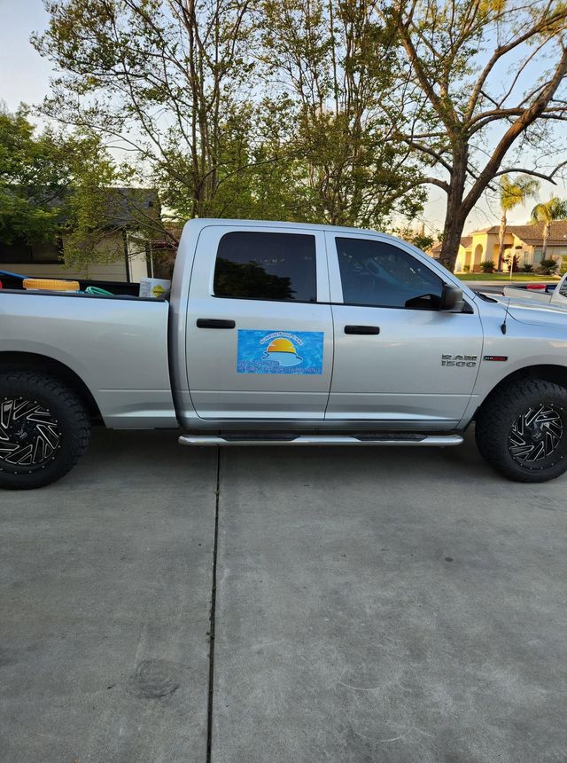 Silver pickup truck parked in a driveway, with a blue logo on the door and trees in the background