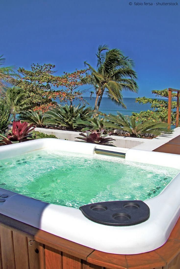 Small white hot tub with bubbling green water on a sunny tropical deck, palm trees in the background