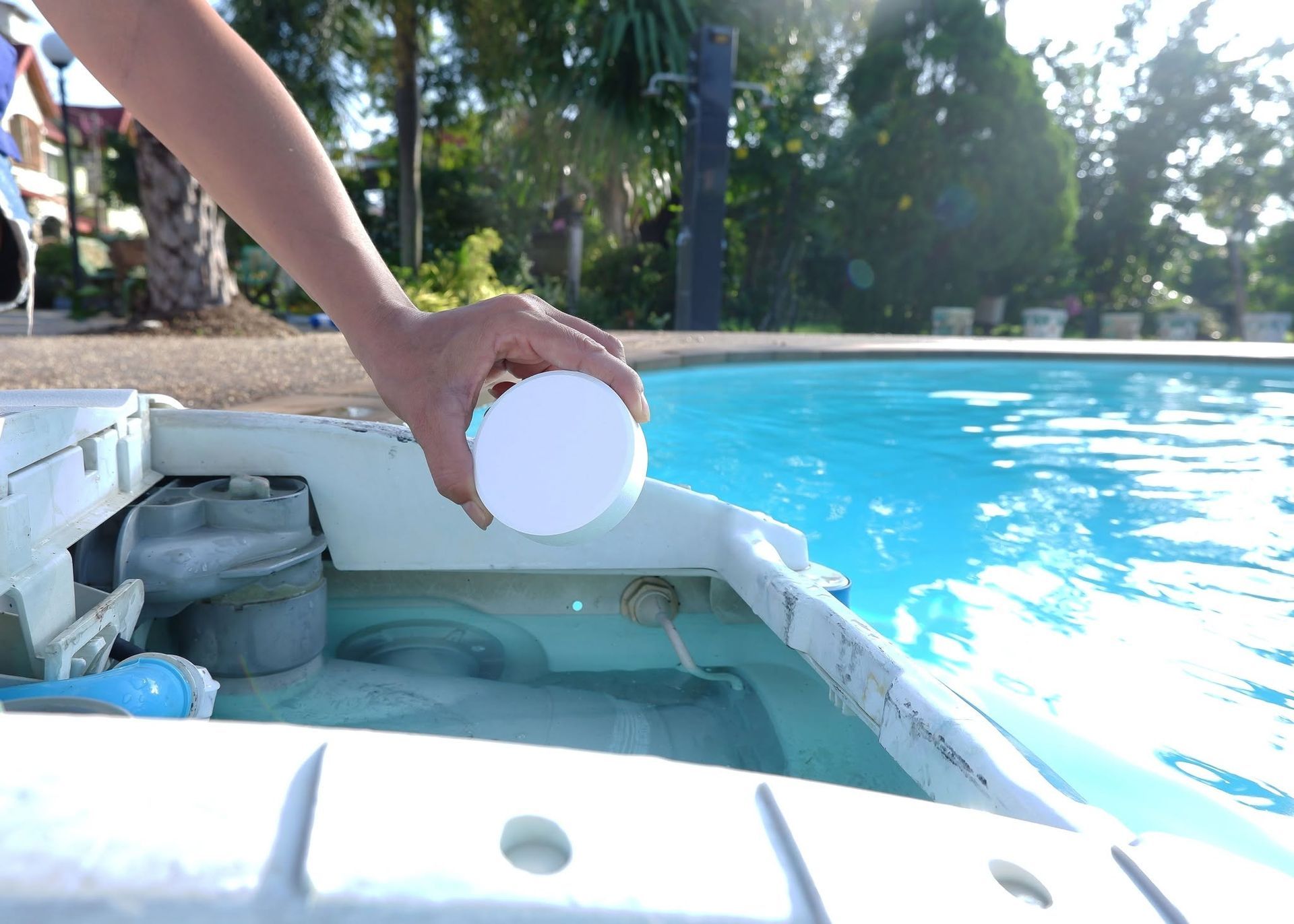Hand placing a white float ball into a hot tub beside a bright blue swimming pool